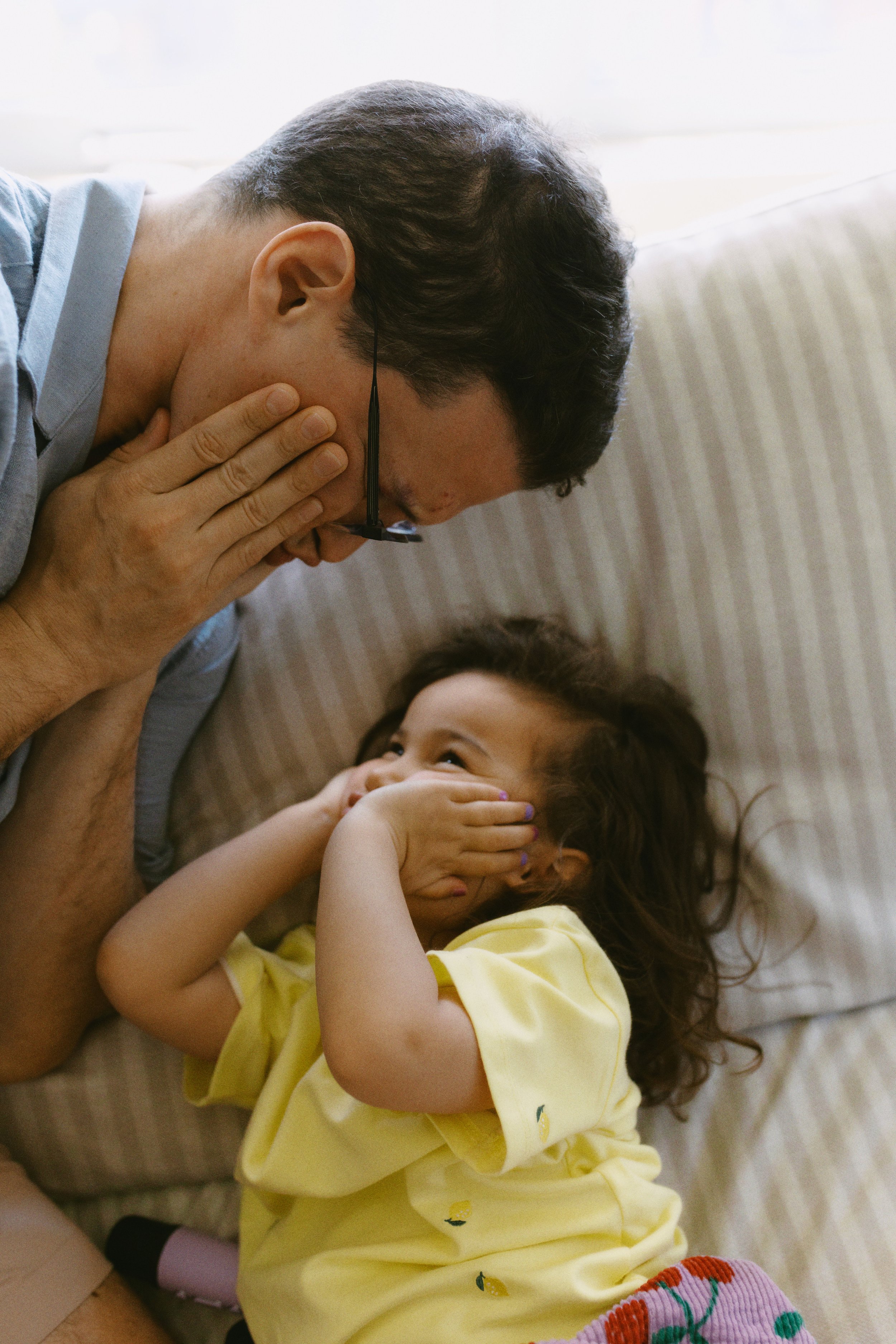 Candid family photo of a father and daughter laughing together on the couch during an in-home family photography session.