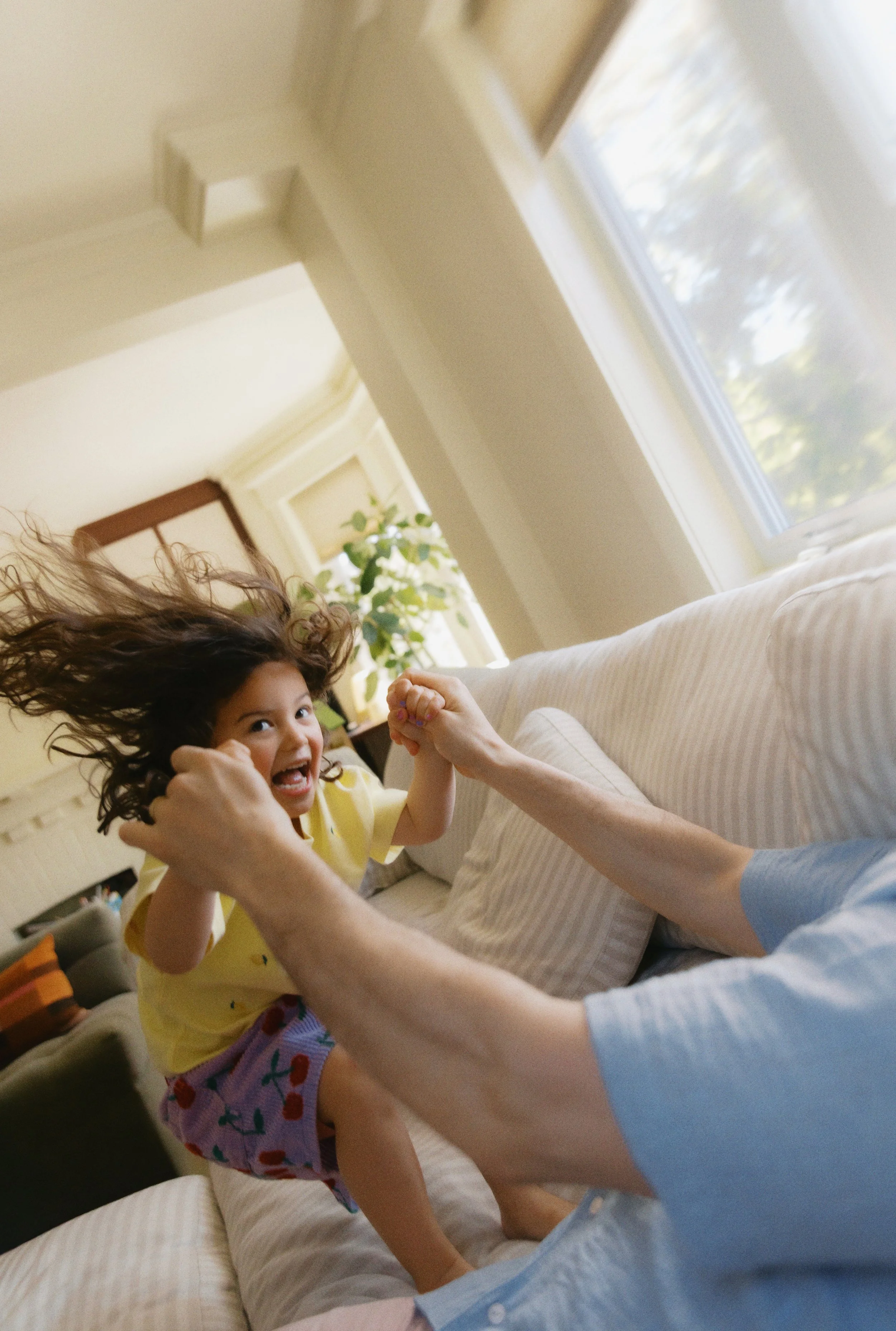 Natural family photo of a father playing with his daughter on the couch during a relaxed in-home session.