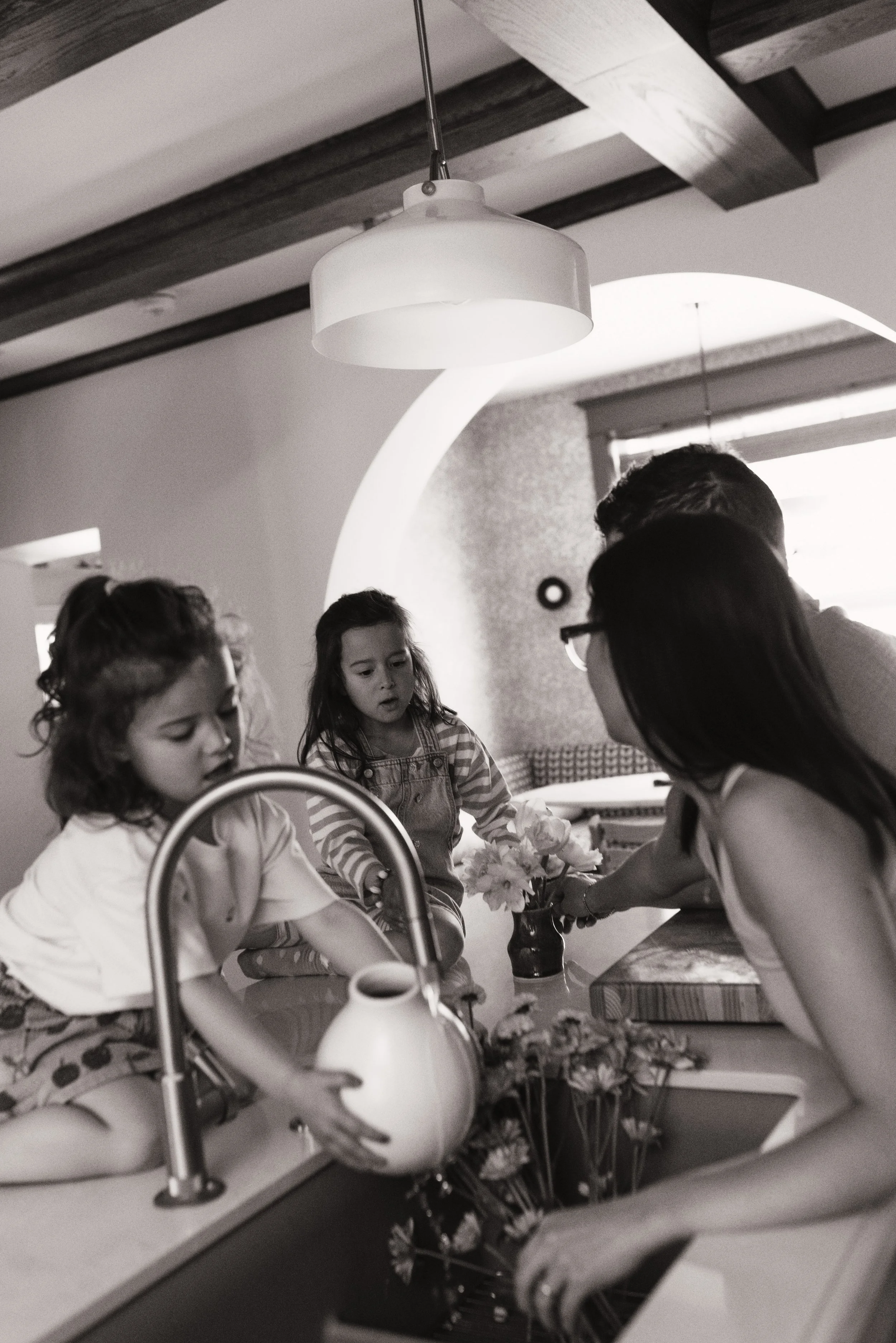 Black and white candid family photo of children and their mother arranging flowers in the kitchen at home.