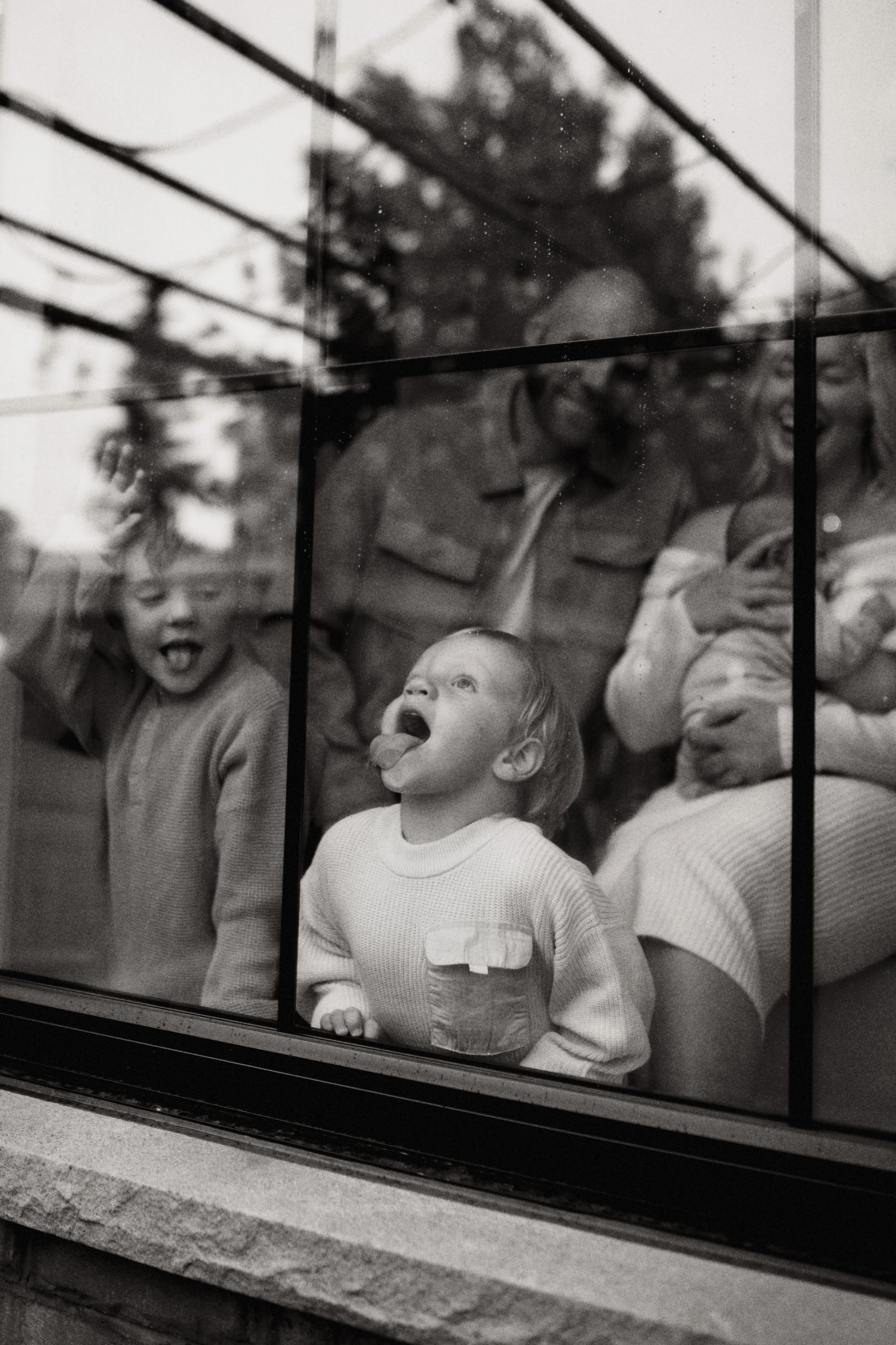 Children looking through a store window, with one child sticking out his tongue, in black and white.