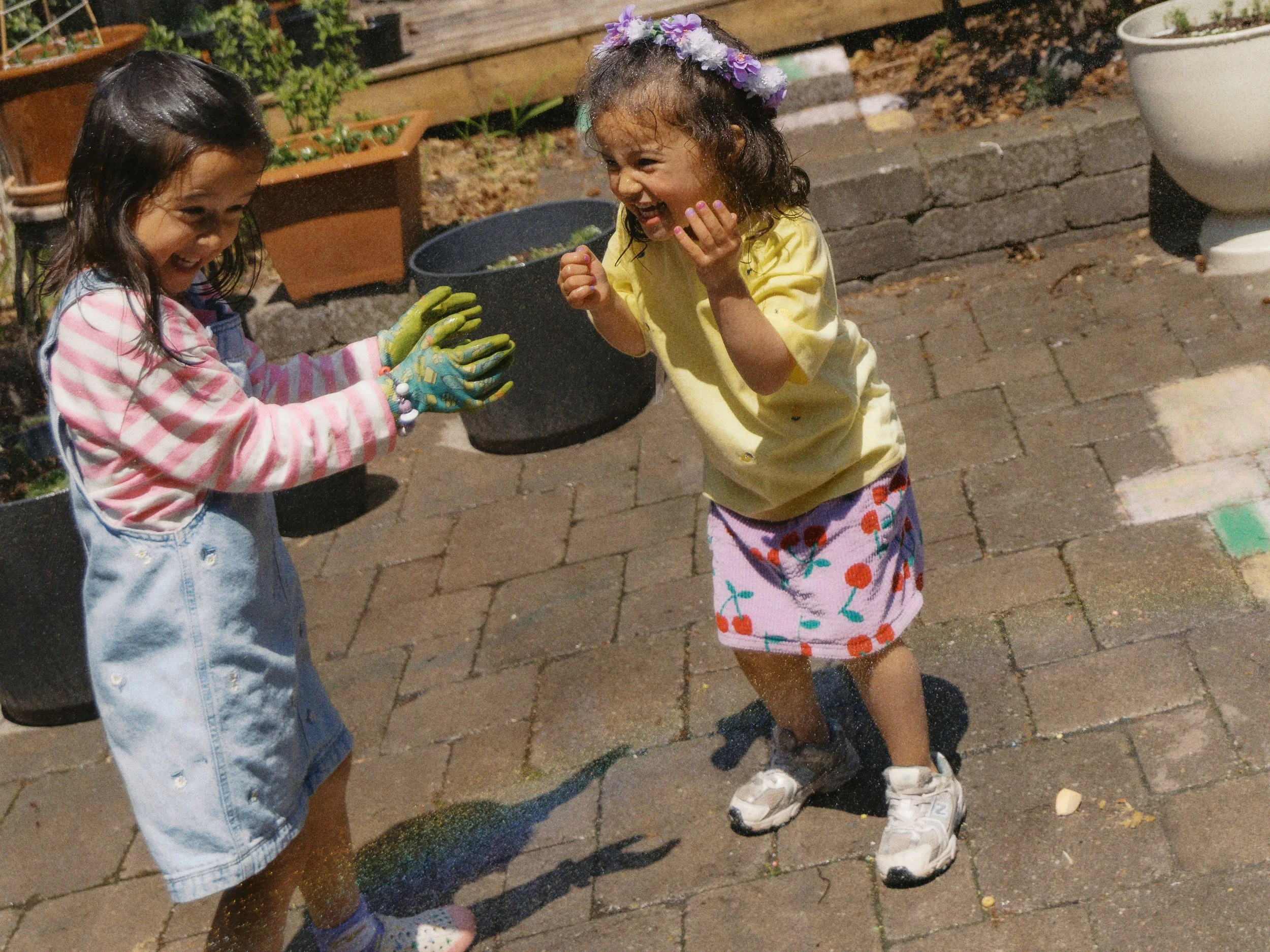 Candid family photo of two children laughing while playing with water in the backyard.
