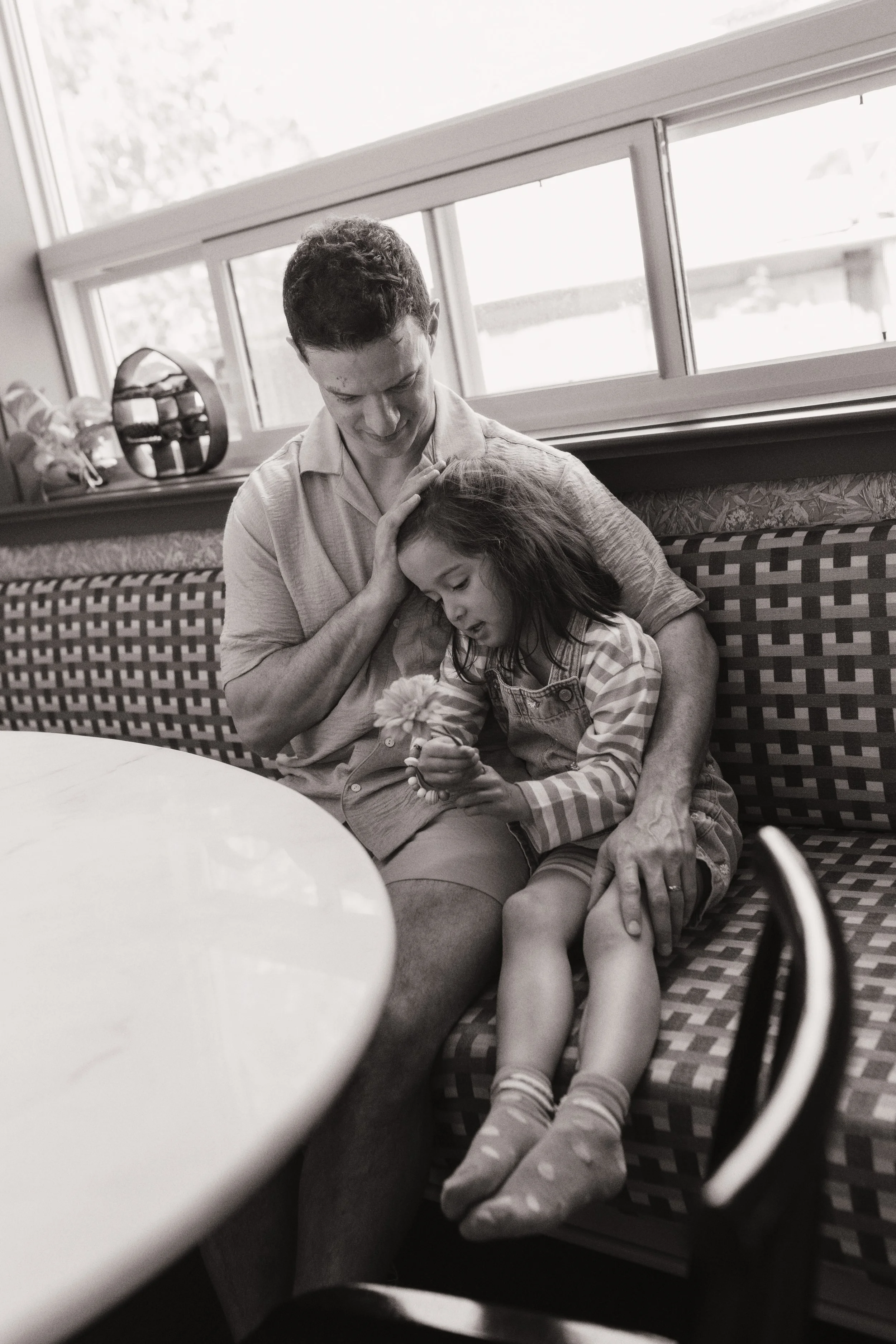 Black and white family photo of a father and daughter sharing a quiet moment at home.