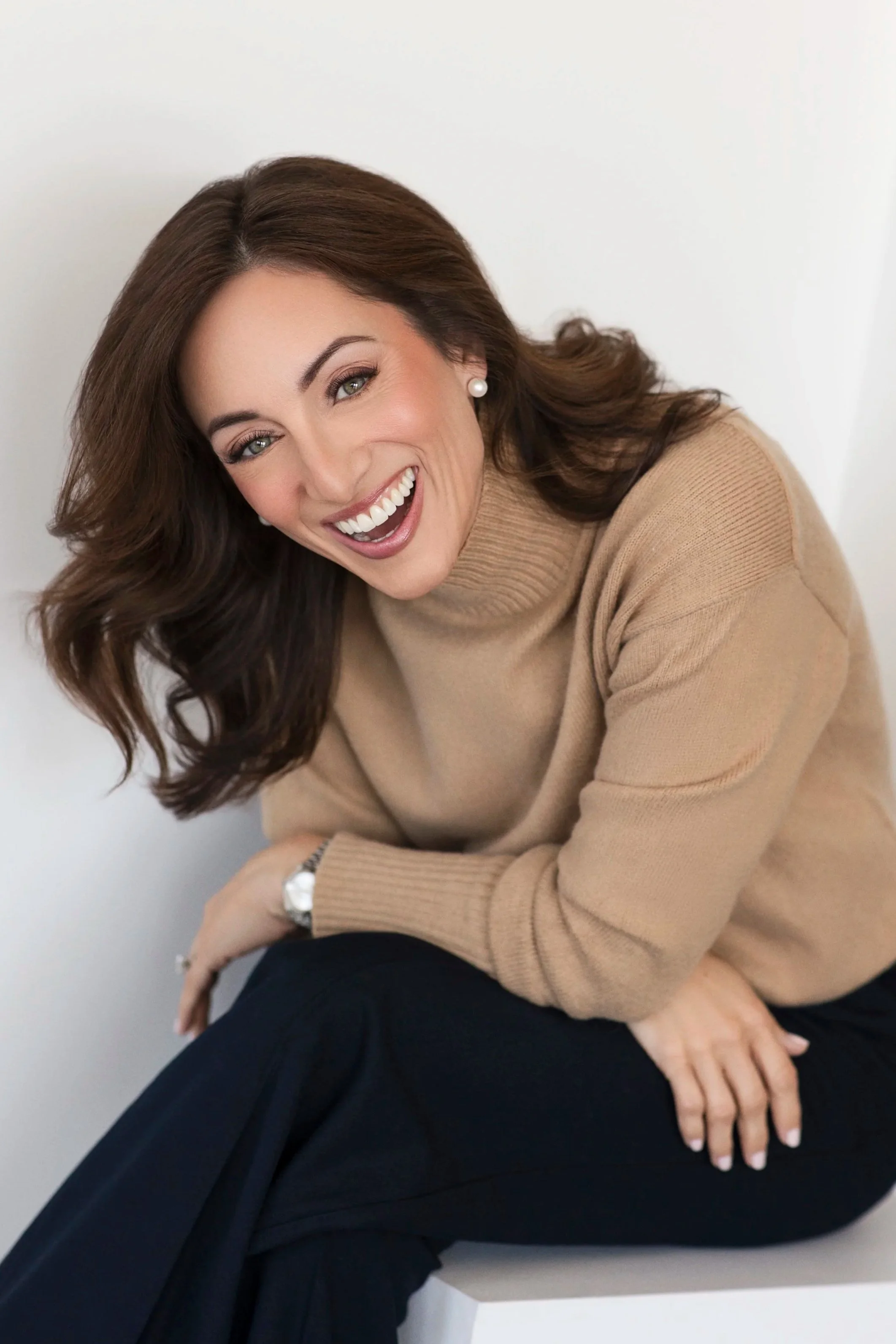 Woman sitting on a posing block in a camel sweater smiling for camera during her branding and headshot photoshoot