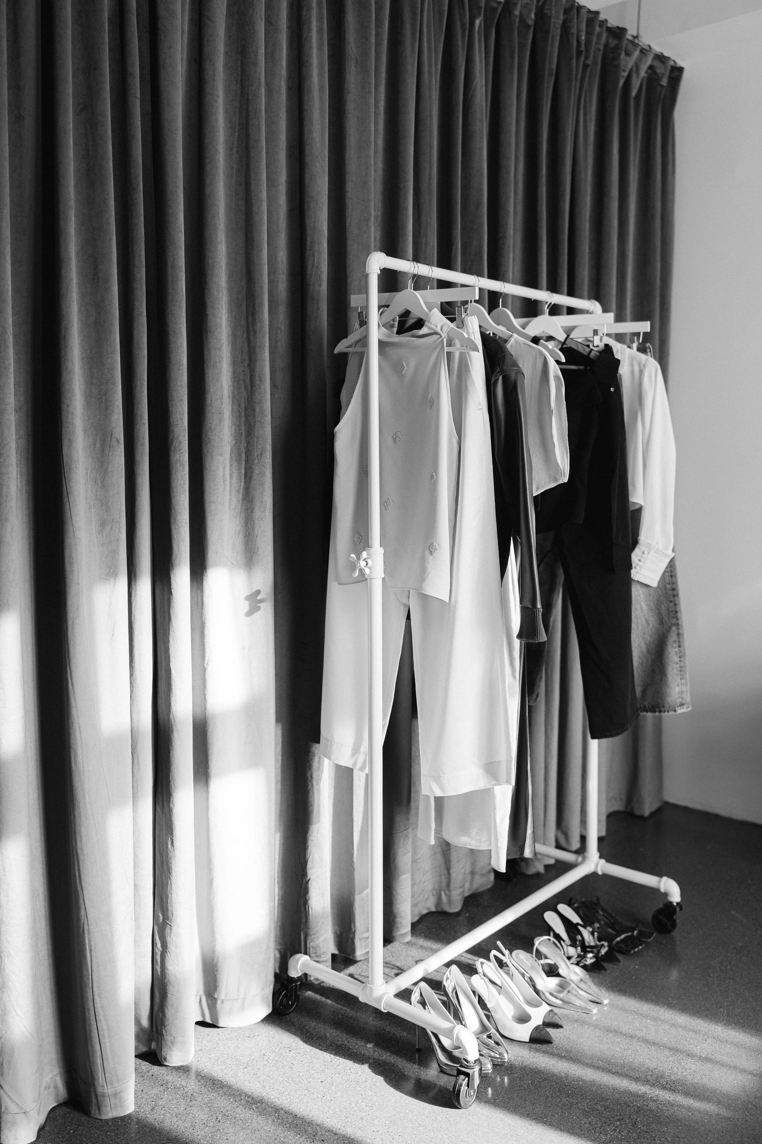 Image of Clothing rack with various garments and shoes underneath, set against a curtain background.