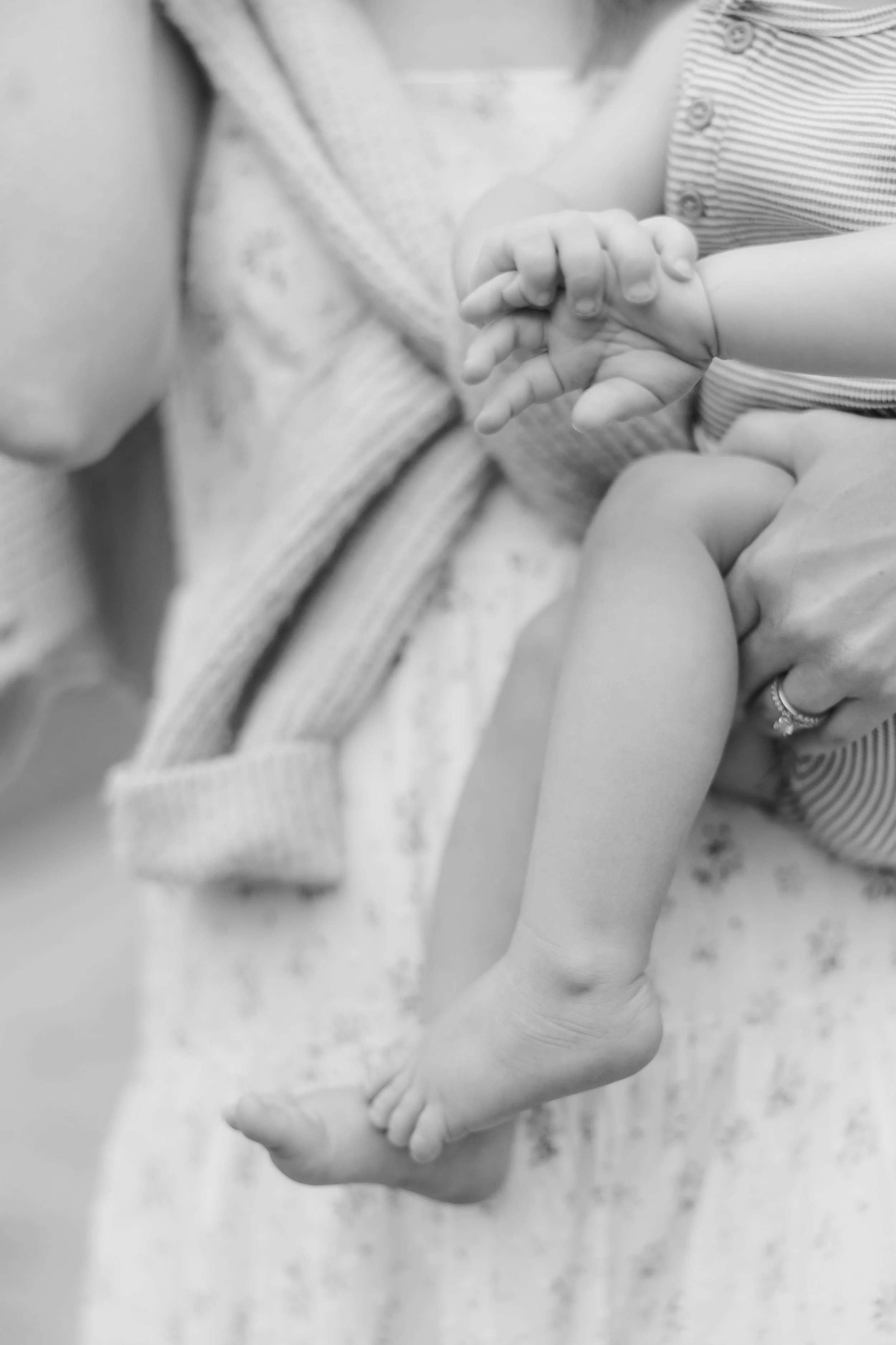 A black and white photo of a mom holding son with a focus on his hands and feet