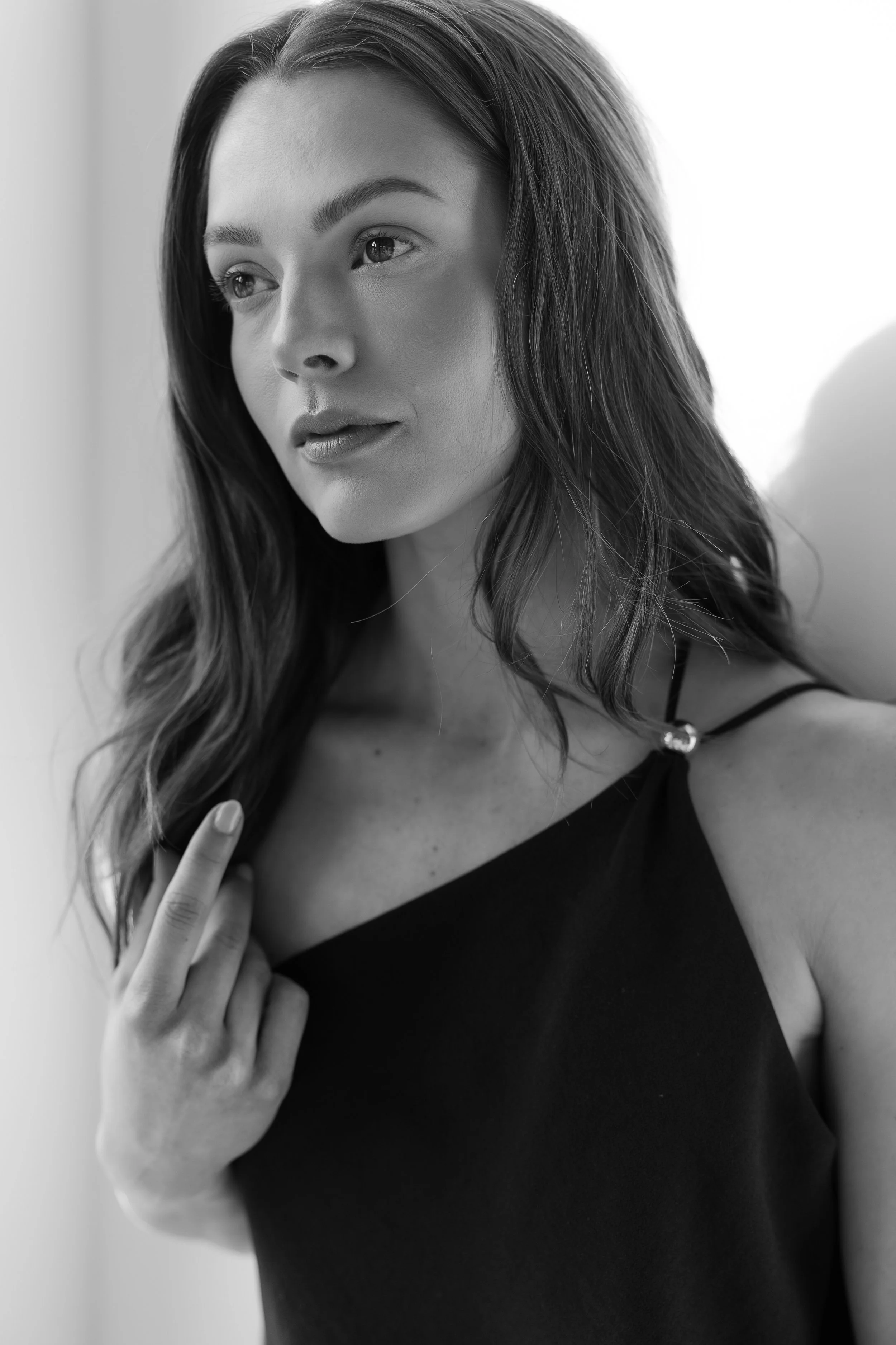 A black-and-white portrait of a woman with long wavy hair, wearing a sleeveless top, looking thoughtfully to the side.