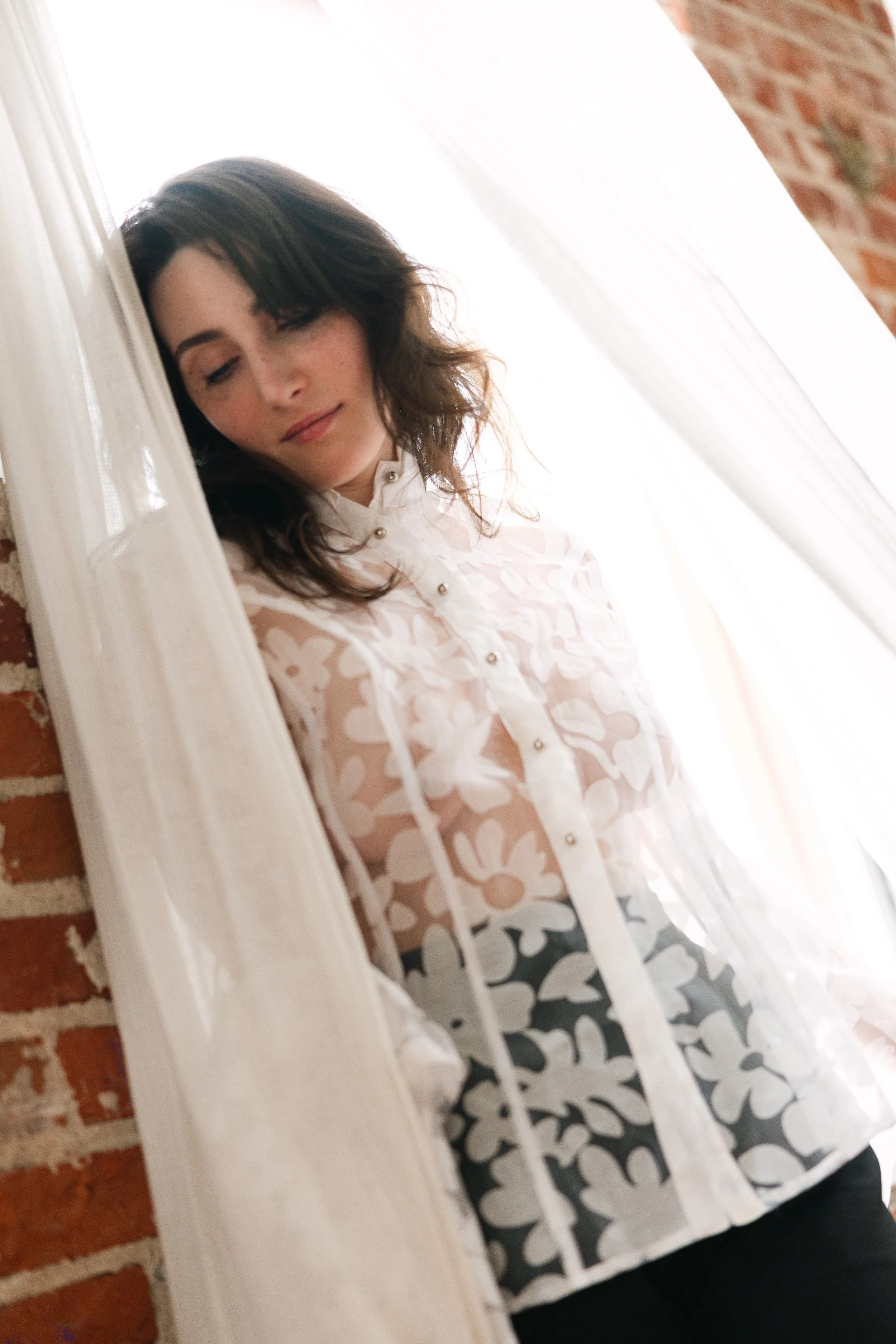 Women standing in a studio with brick walls and curtains, looking down