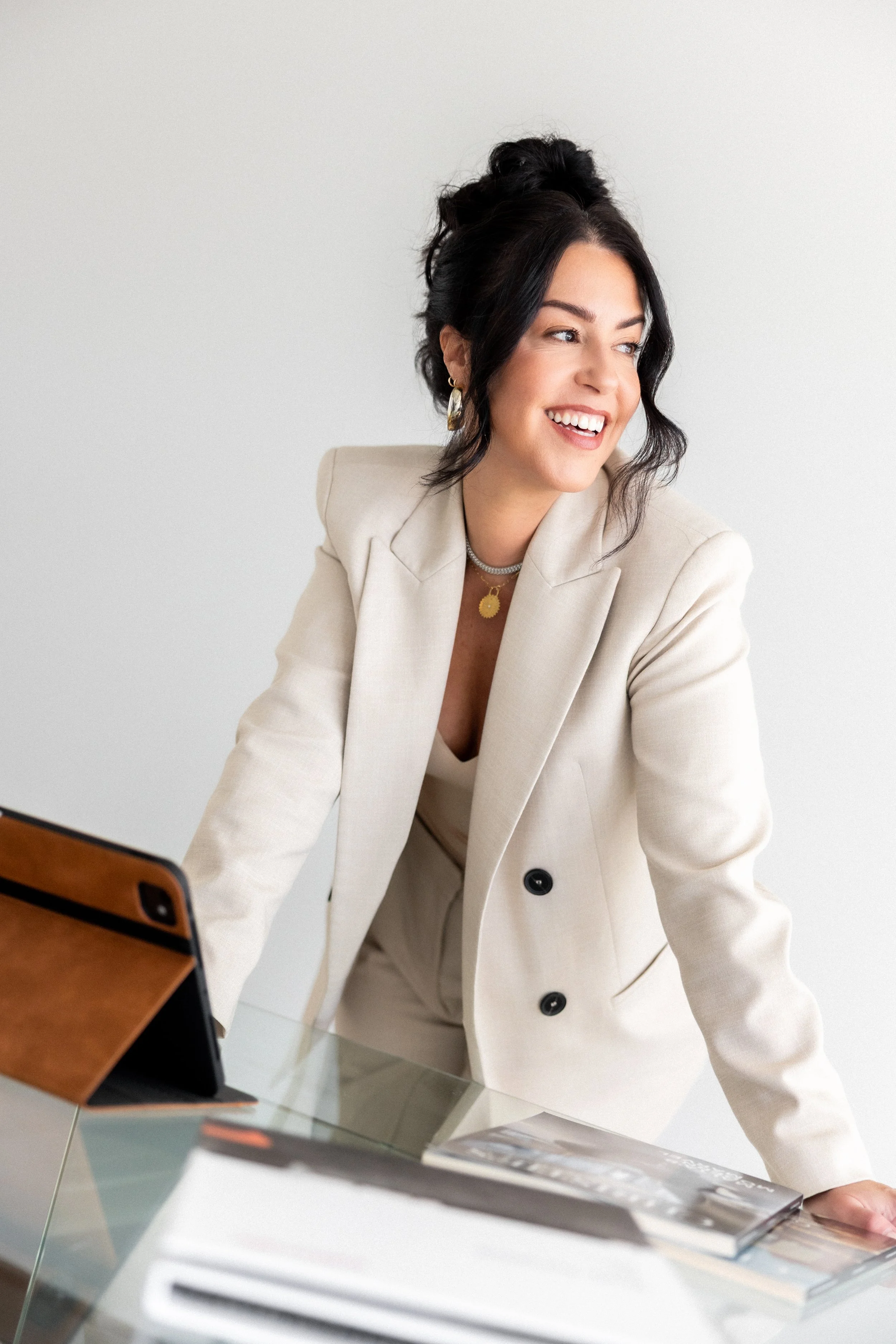 Women in a suit standing at desk smiling with her iPad