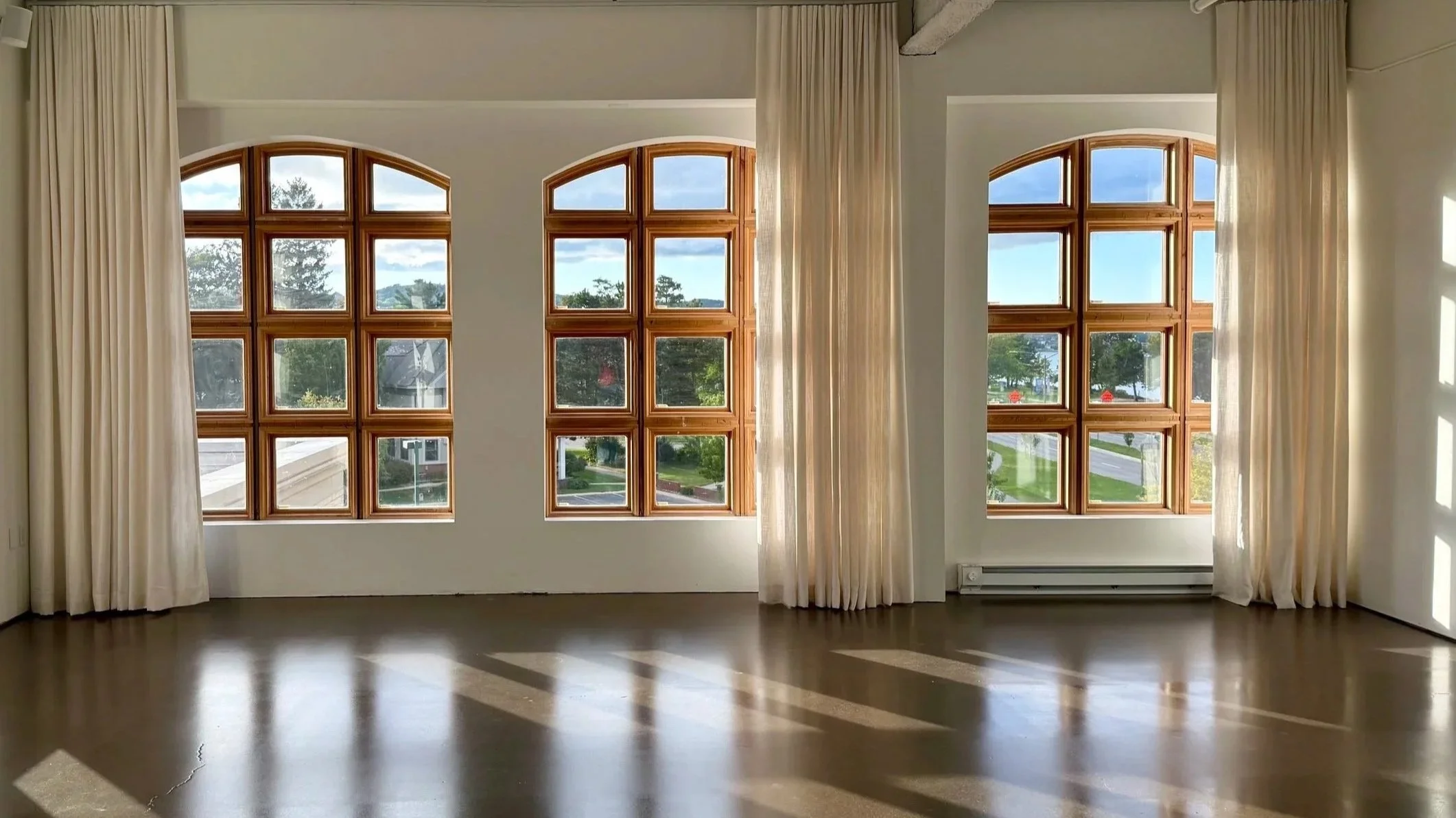 A photo of large arched windows with beautiful curtains and sun beaming through with natural light