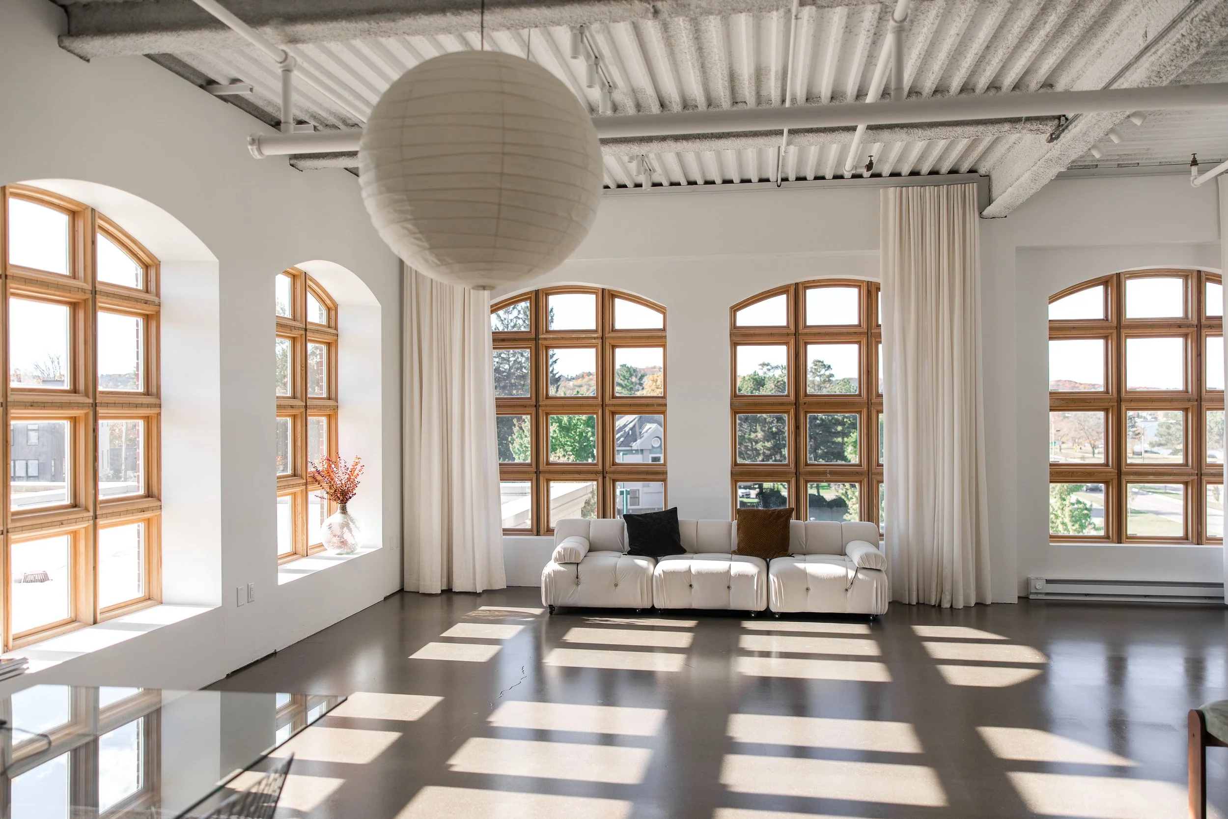 Image of bright photography studio with large arched windows, white curtains, and concrete floors