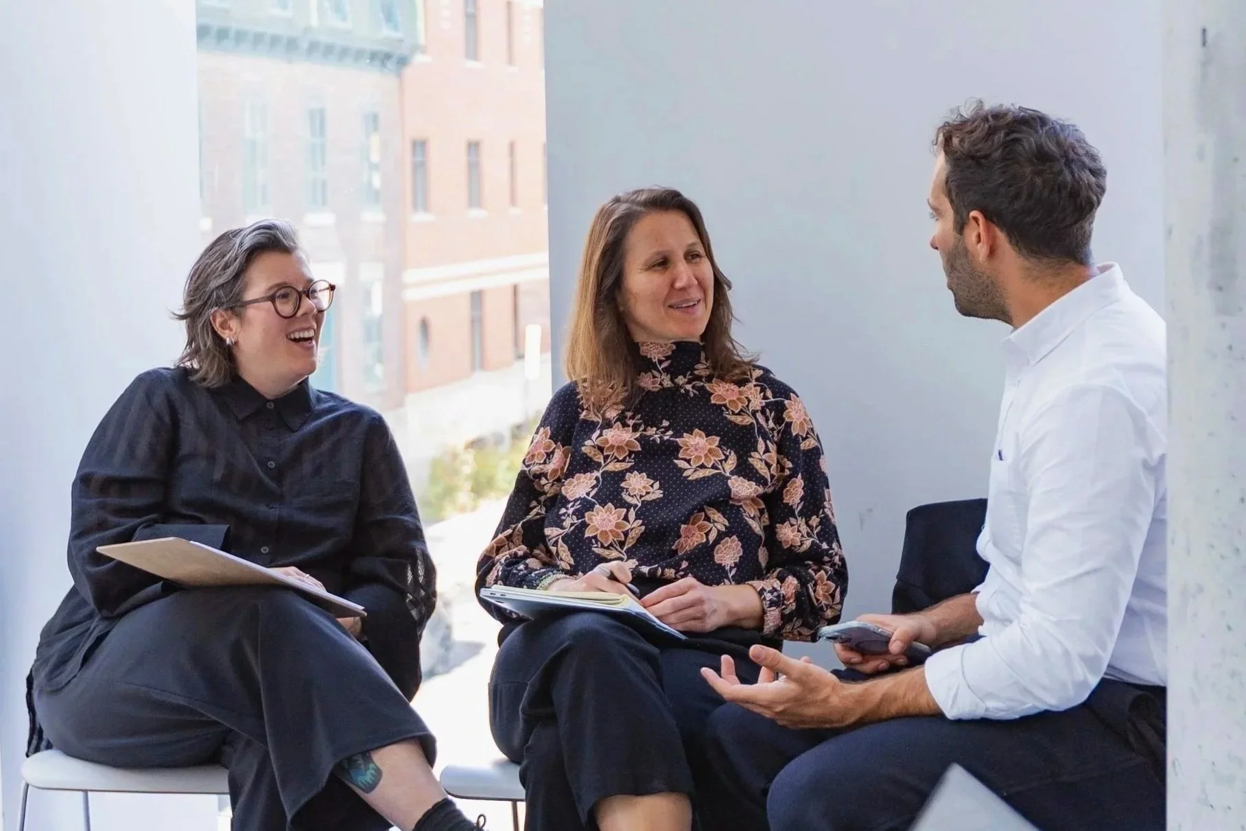 Trois membres d’Estuaire discutent assis près d’une grande fenêtre, carnets en main.