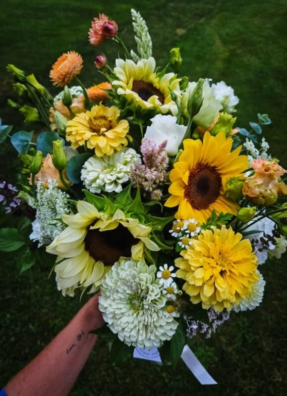 A bouquet of mixed summer flowers including sunflowers, dahlias, daisies, and various greenery.