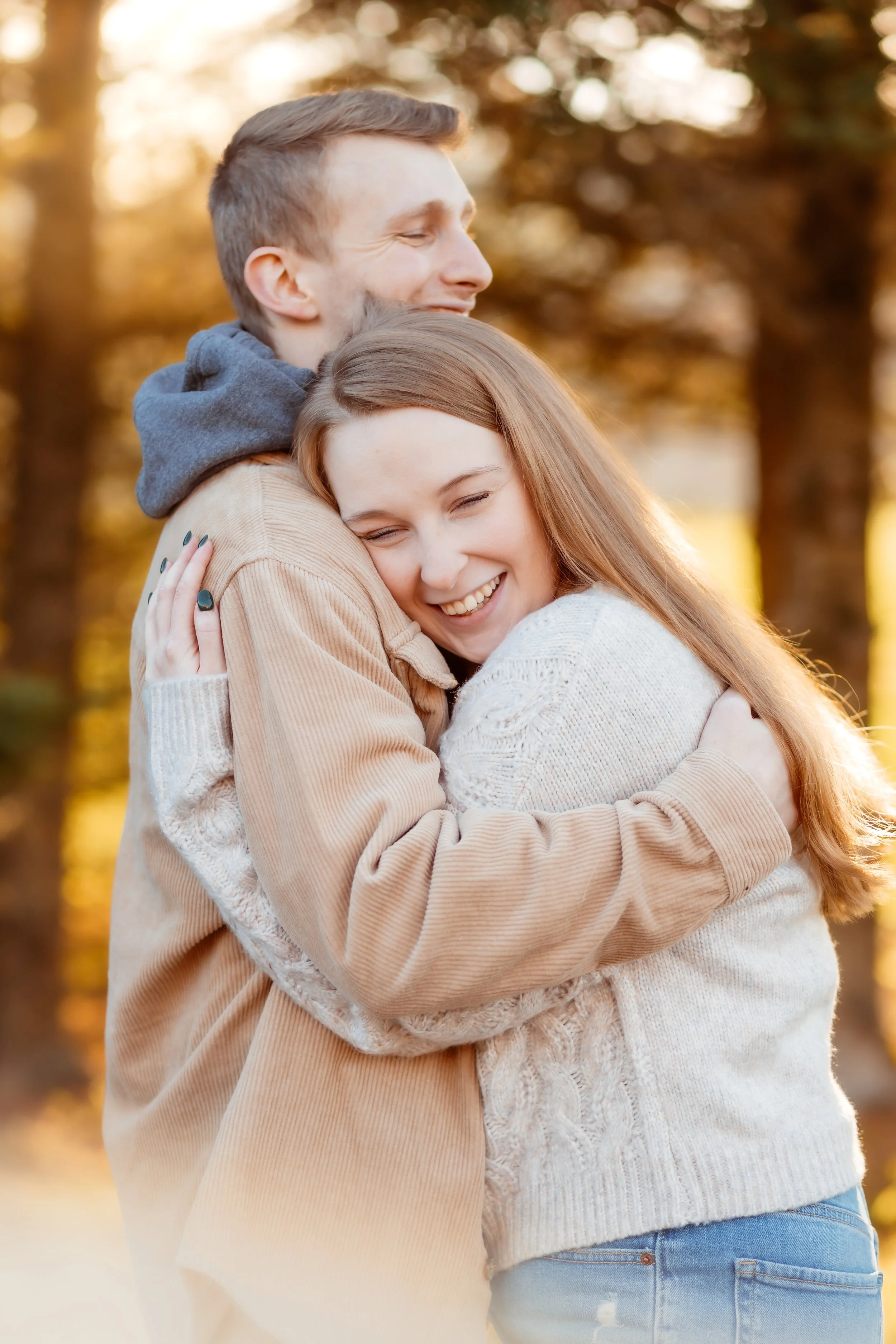 A happy young couple hugging outdoors during autumn, with trees and sunlight in the background.