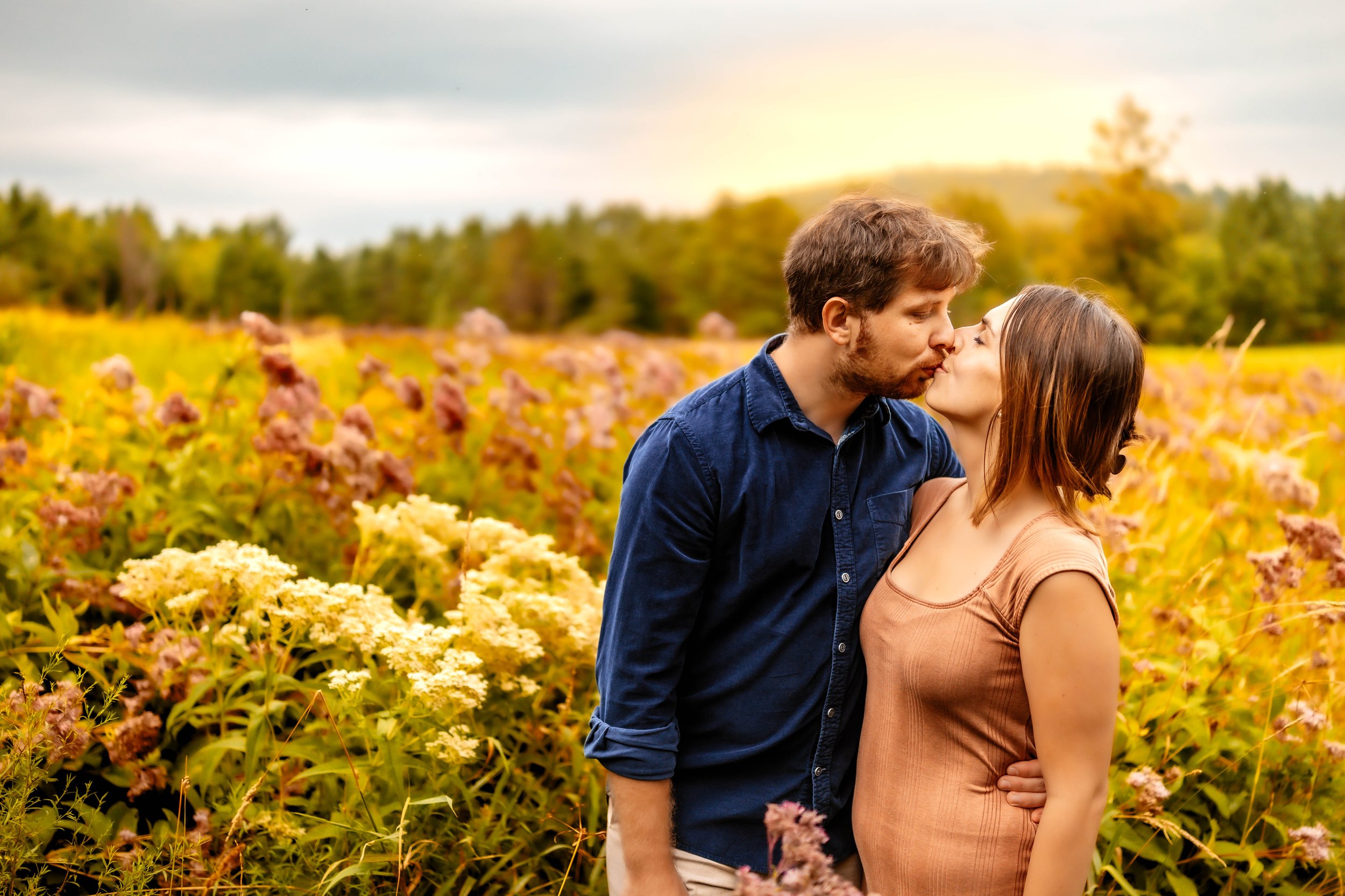 A couple in an embrace and sharing a kiss in a colorful flower field during sunset.