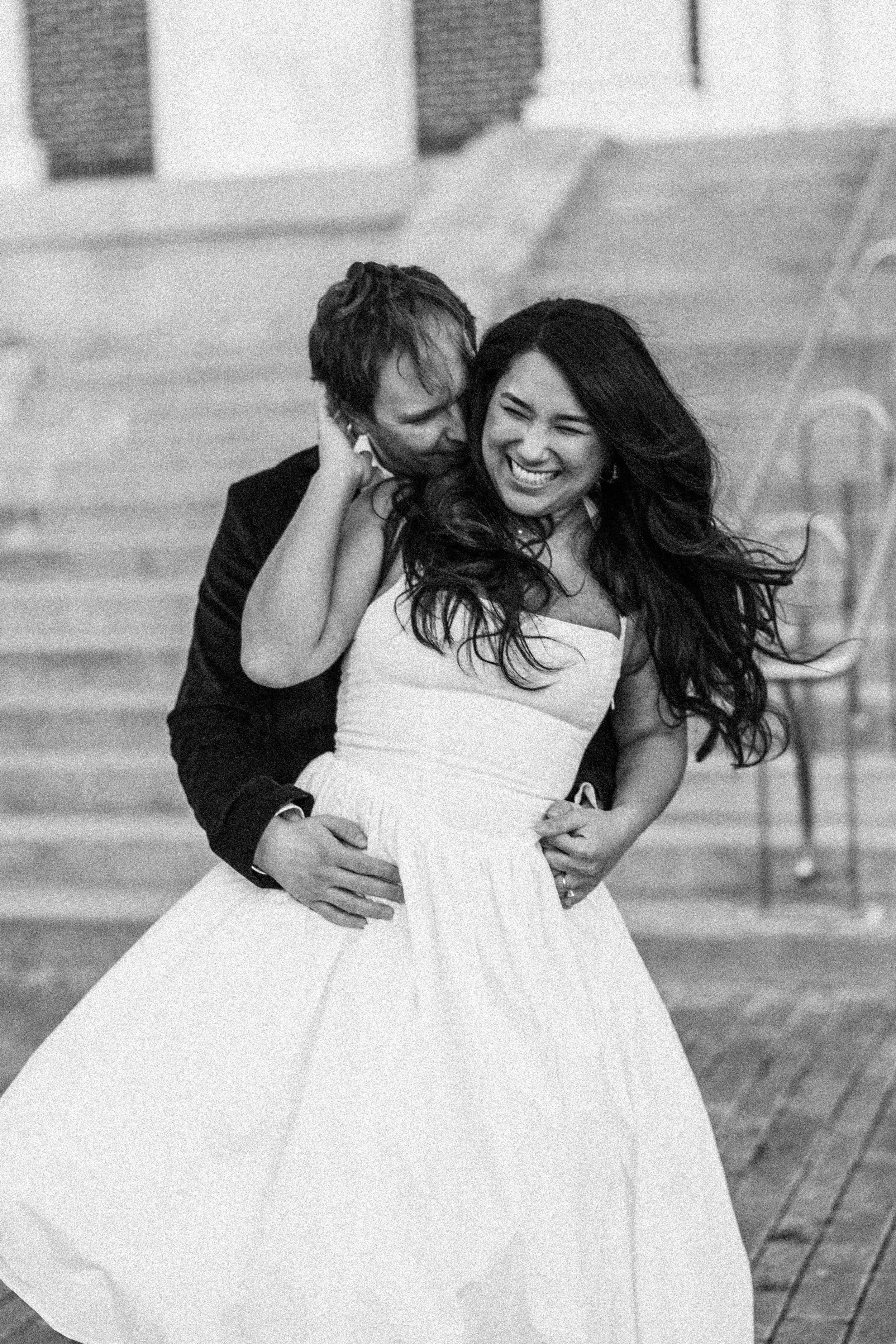 A joyful couple dancing on stairs, the woman in a white dress and the man in a dark suit, sharing a happy moment.