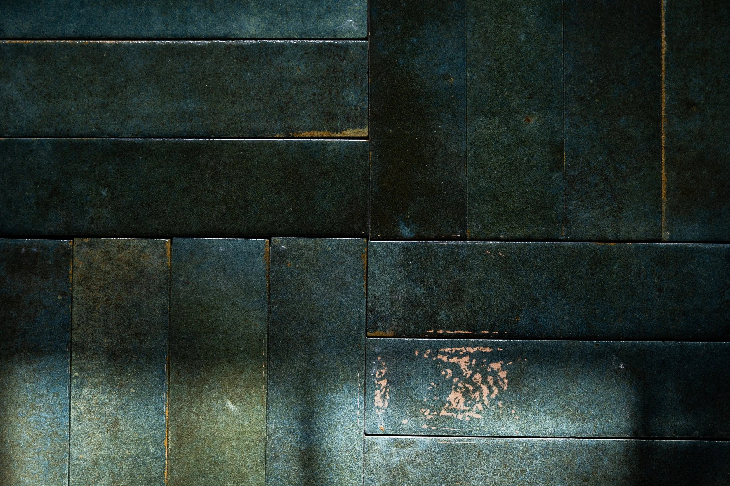 Close-up of dark stone sauna tiles arranged in a rectangular pattern, showing some weathering and slight rust stains. The jade color represents grounding.