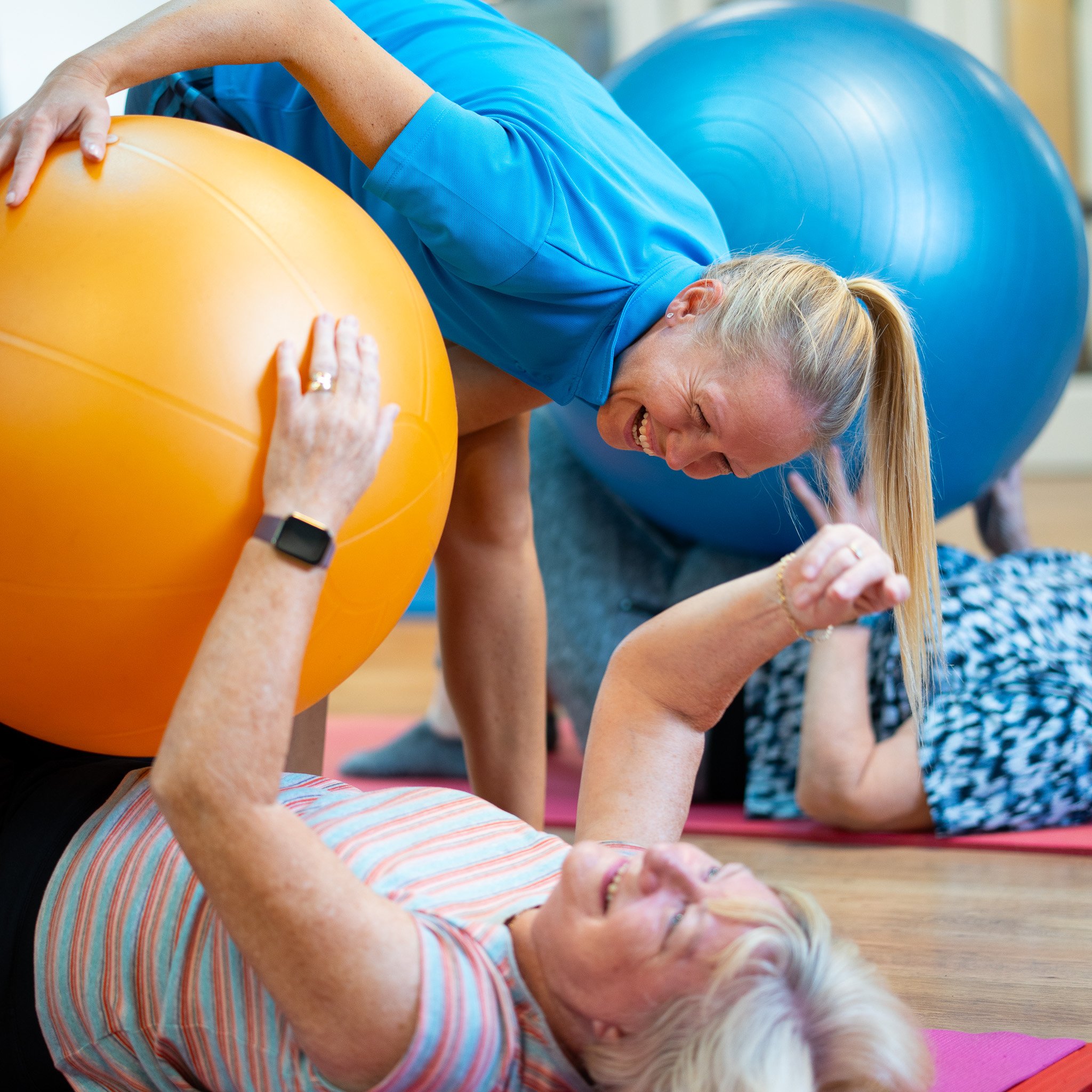 Women participating in a fitness class with exercise balls, laughing and engaging in a playful moment.