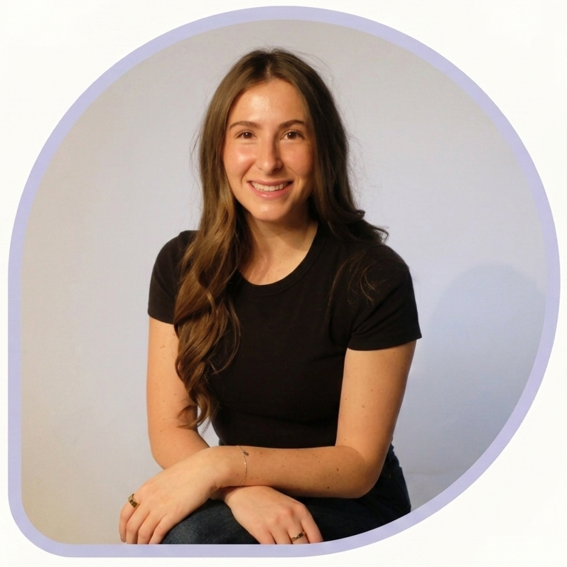 A young woman with long brown hair sitting and smiling, wearing a black t-shirt, against a plain gradient background.