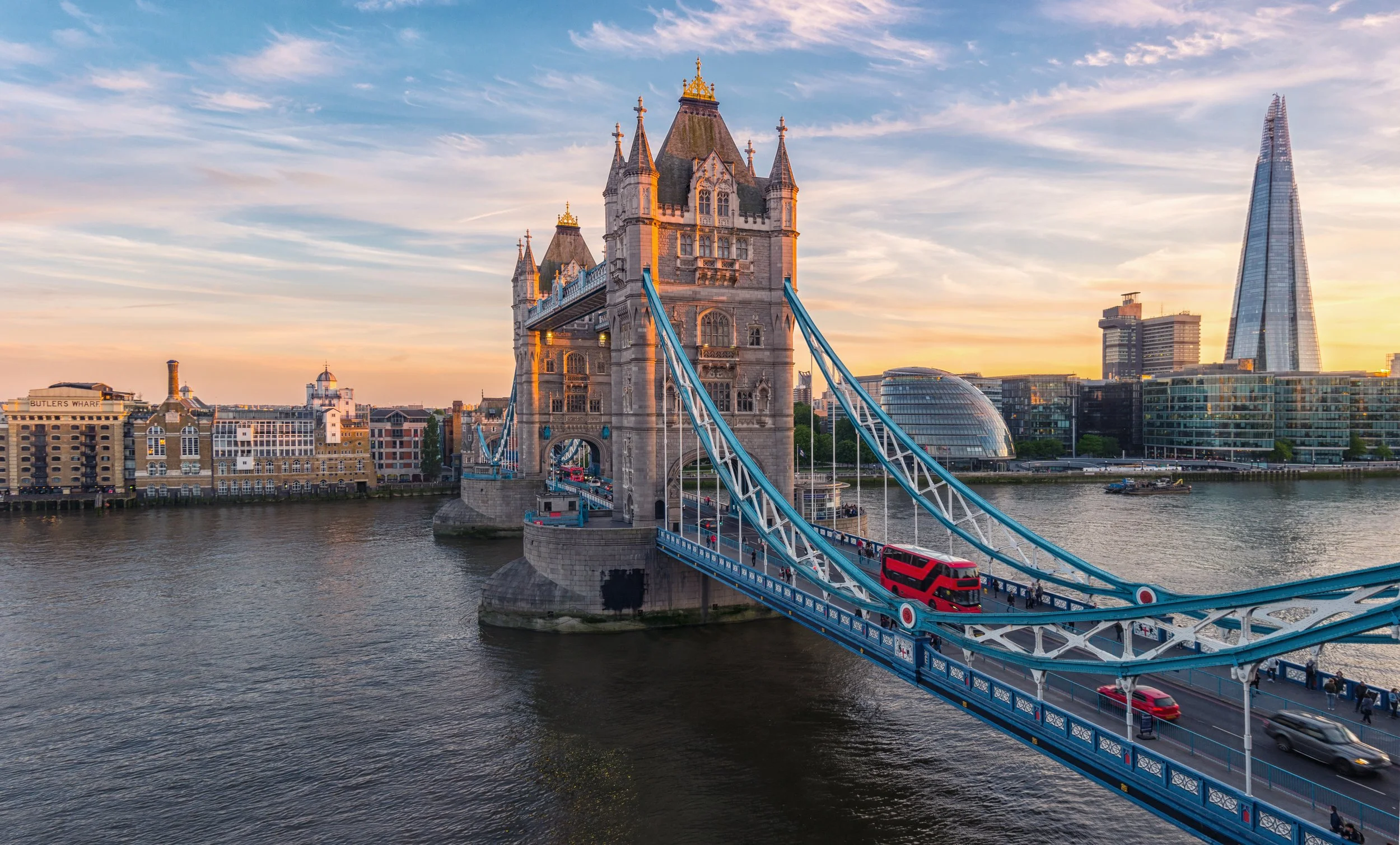 Bilden visar Tower Bridge i London under solnedgången, med trafik på bron och modern stadsskyline i bakgrunden.