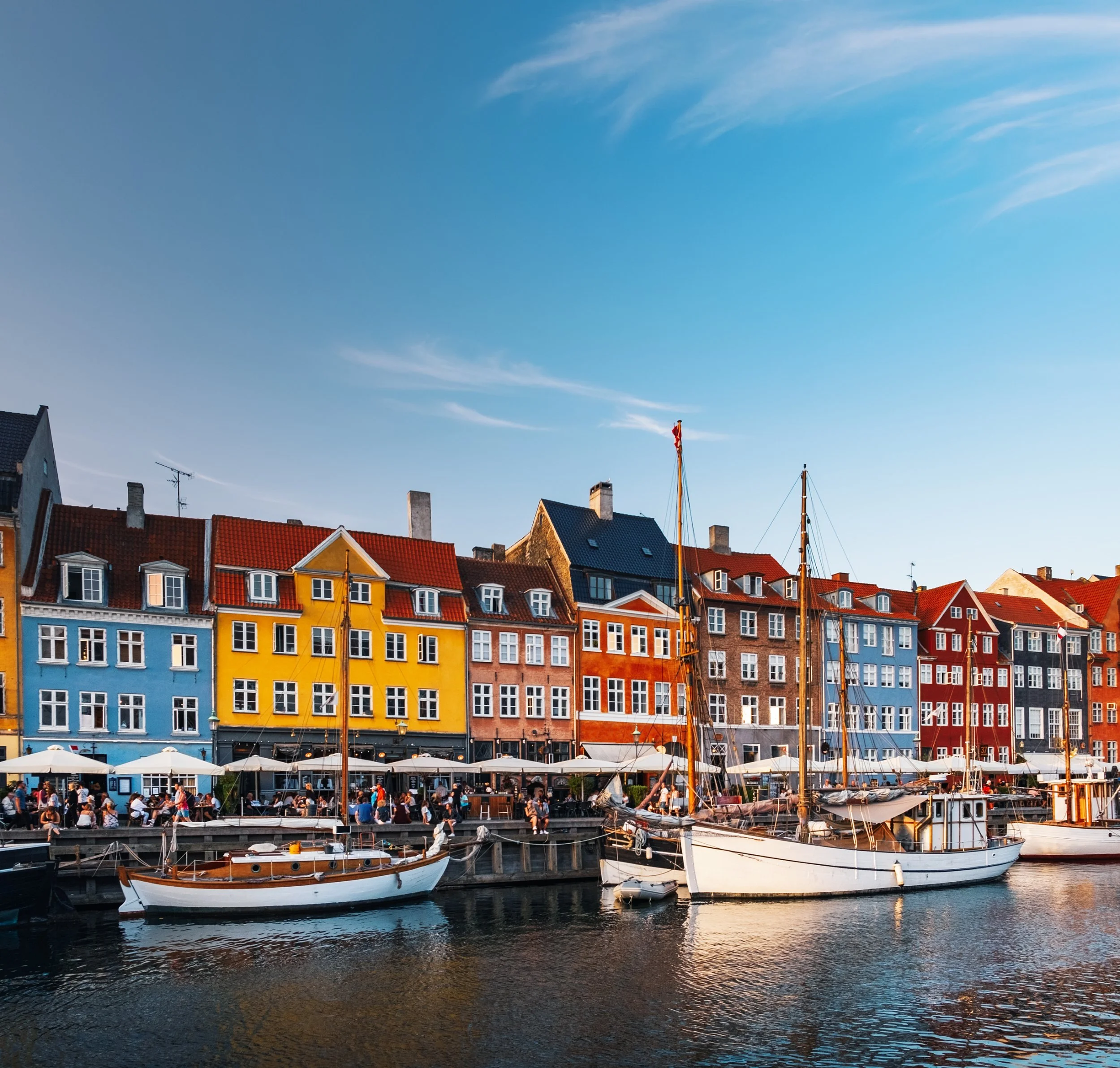 Färgglada hus vid hamnen med båtar i vattnet och människor som äter utomhus.