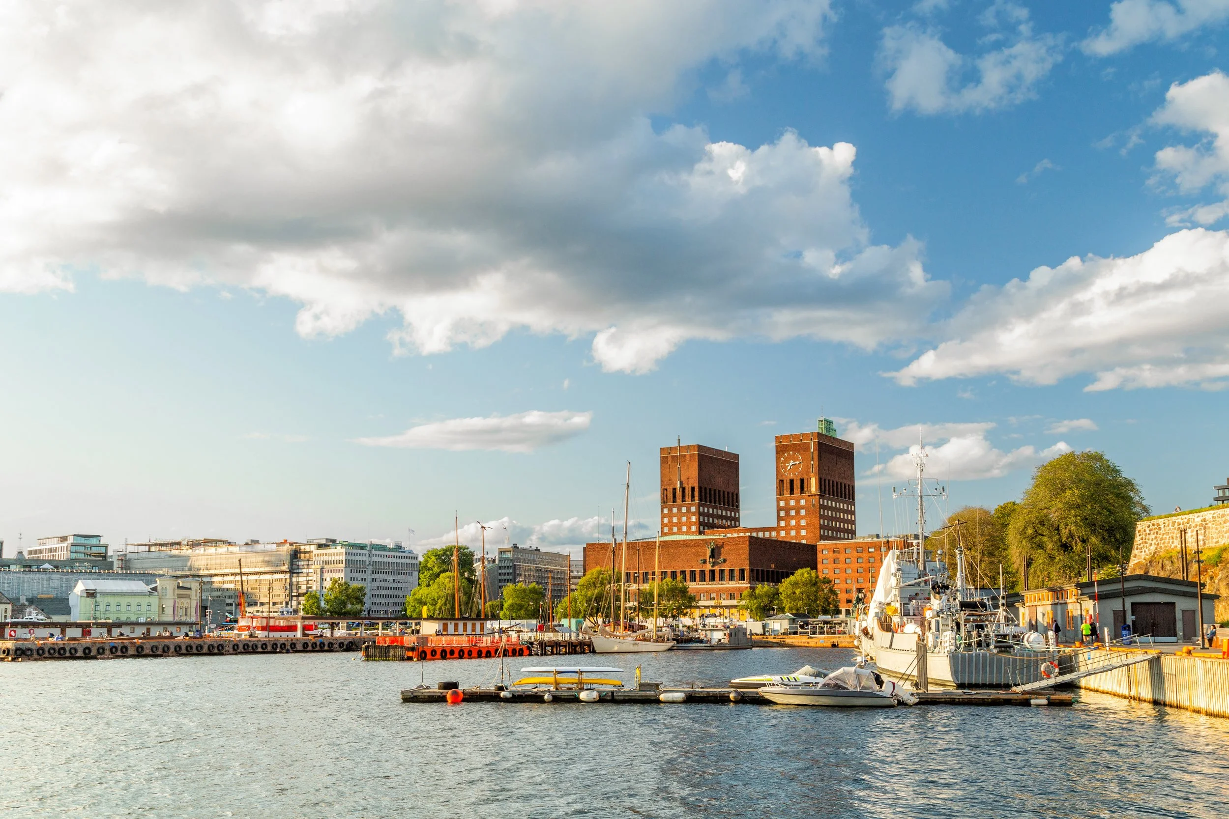 Sjö med båtar framför en stadsskyline med moderna byggnader och en historisk rödmålad byggnad med två torn.