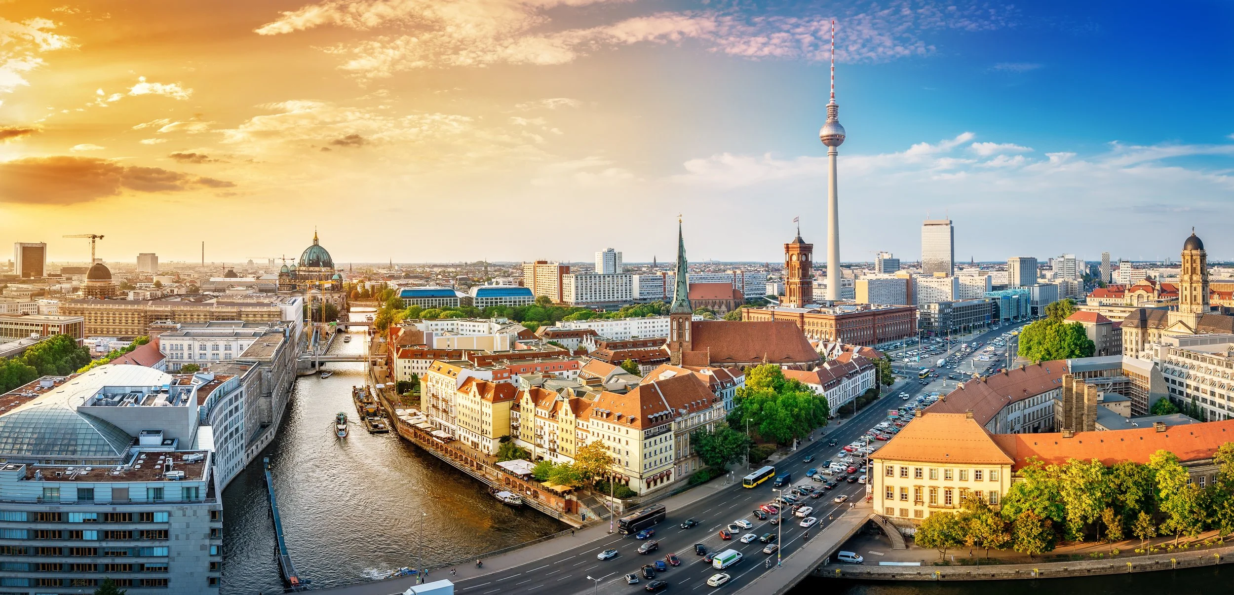 En stadsskyline med floden som rinner genom centrum, tydligkända byggnader inklusive Fernsehturm i Berlin, och en solnedgång i bakgrunden.