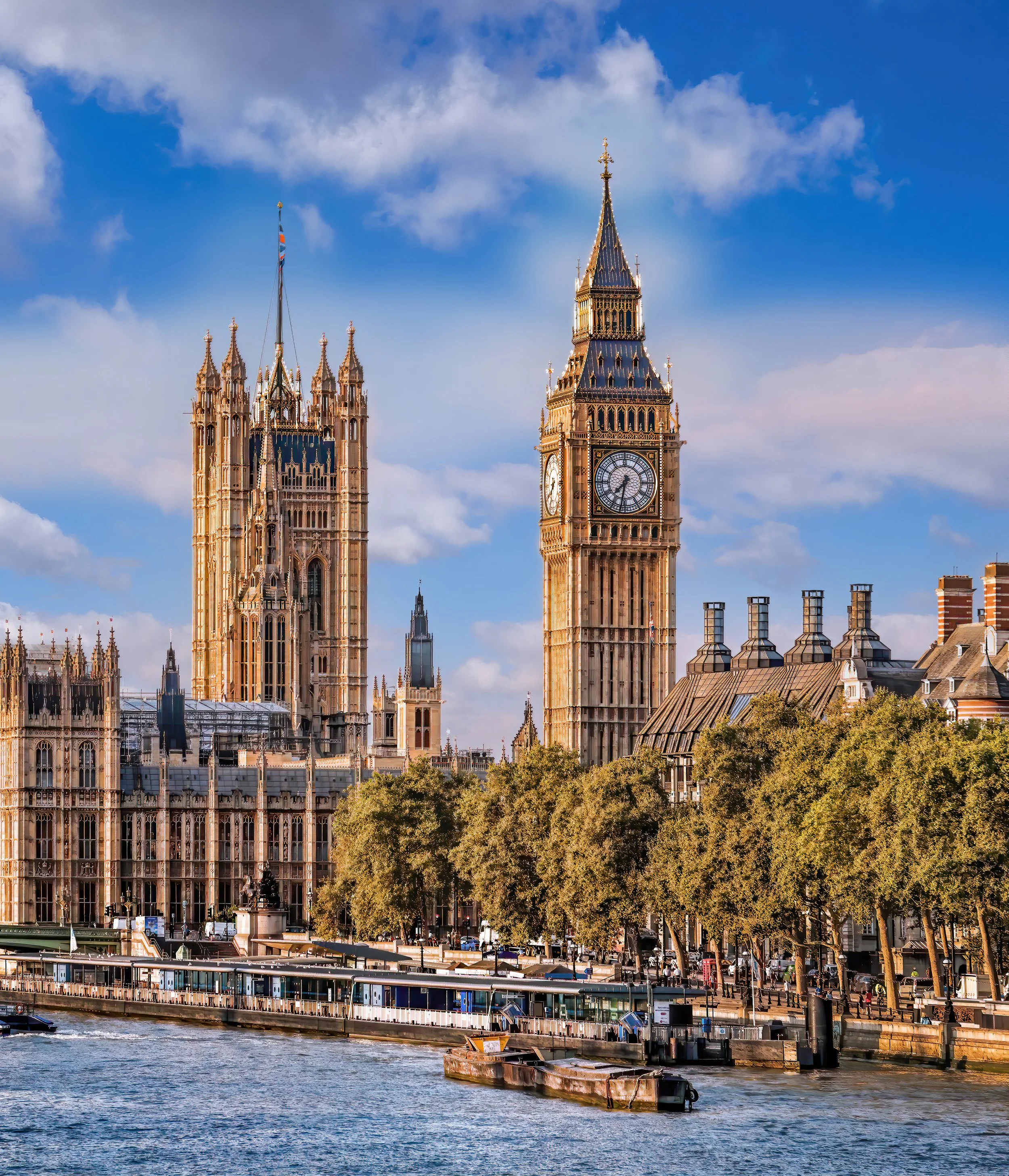 Bilder av Big Ben och Palace of Westminster i London sett från floden Thames på en solig dag med blå himmel och några moln. I förgrunden syns båtar på vattnet och ett kajområde.