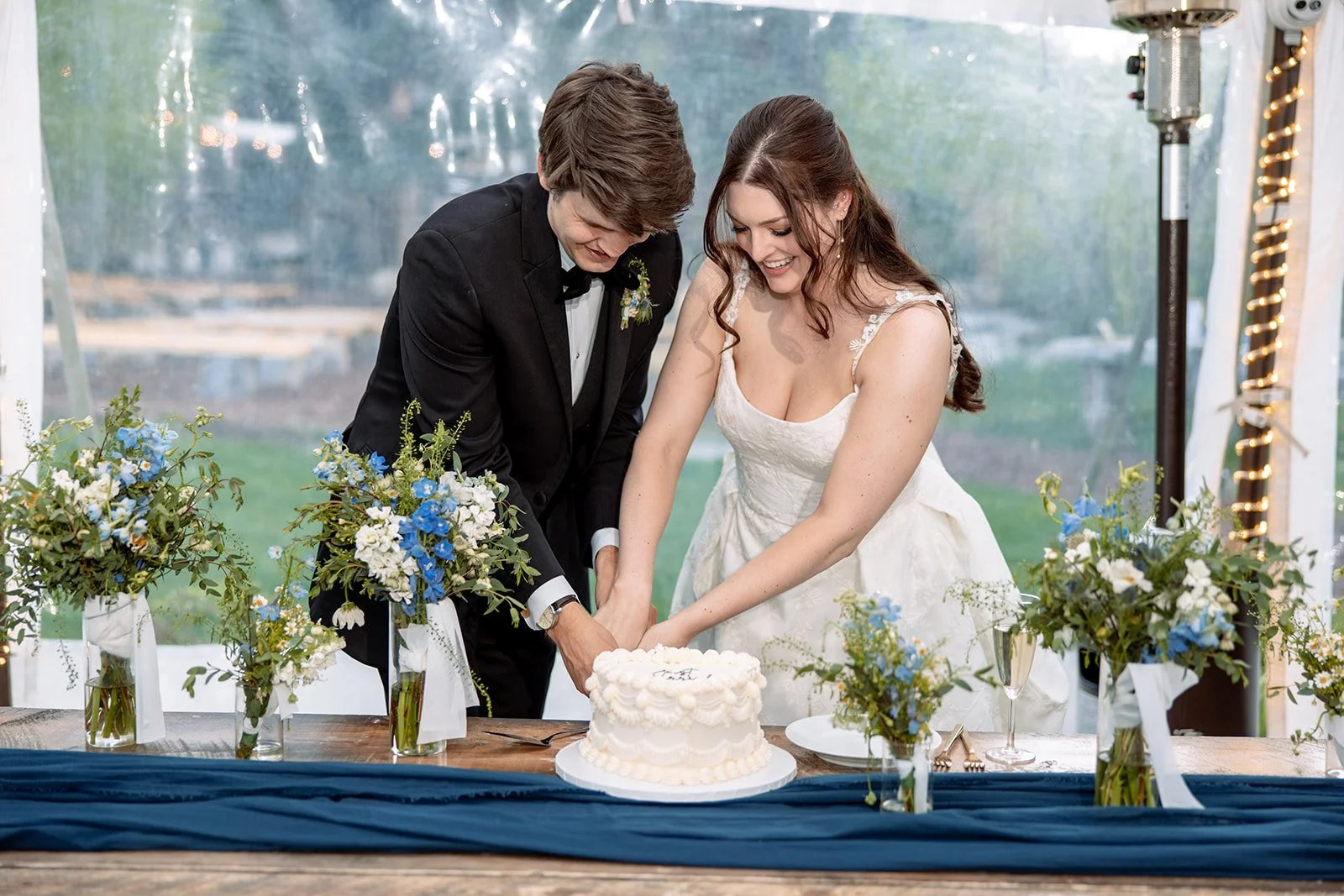 Newlywed couple cutting a decorated wedding cake at a floral reception table