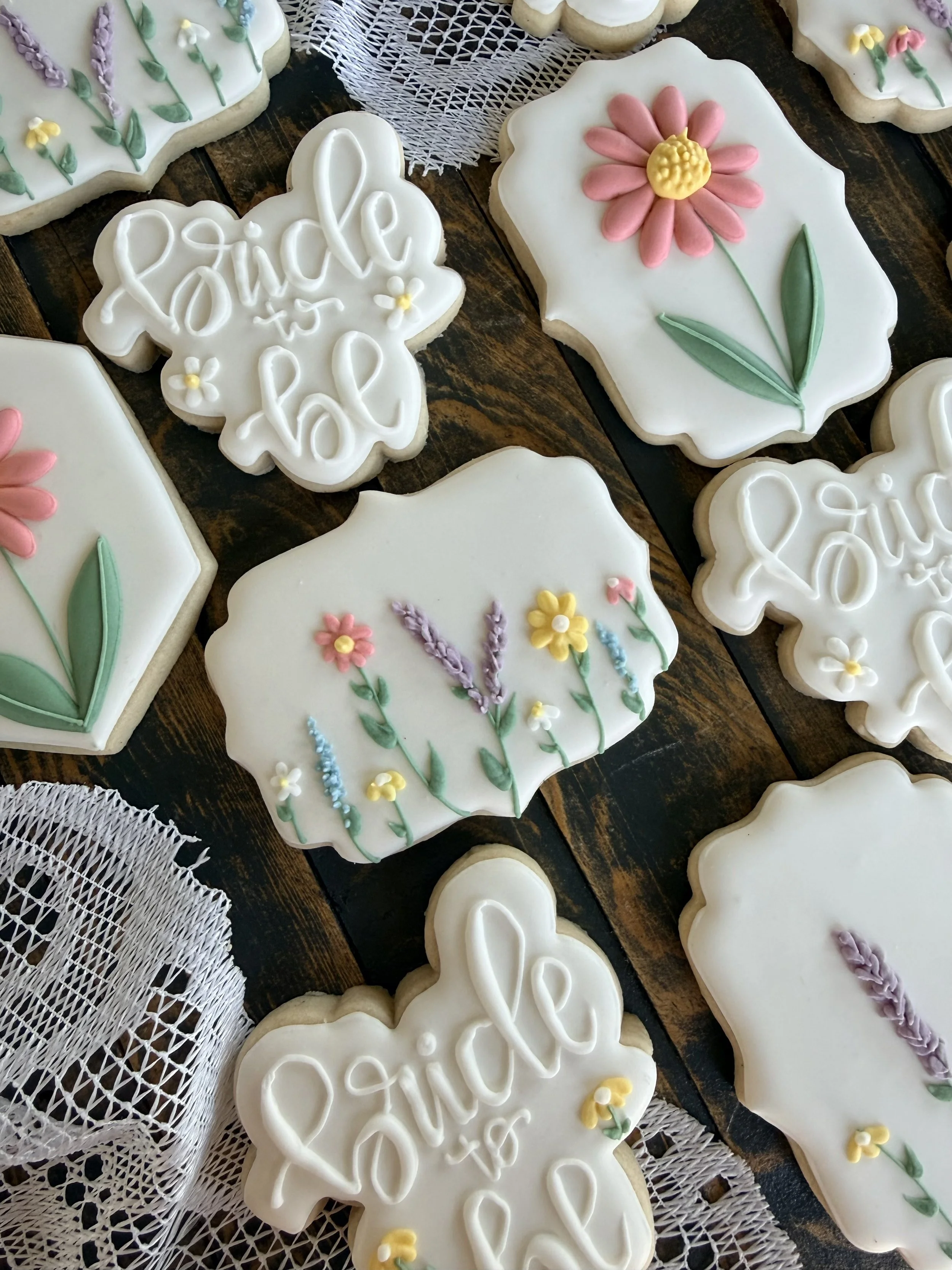 Assortment of white-iced flower-shaped sugar cookies decorated with colorful floral designs and butterfly cookies on a rustic wooden table