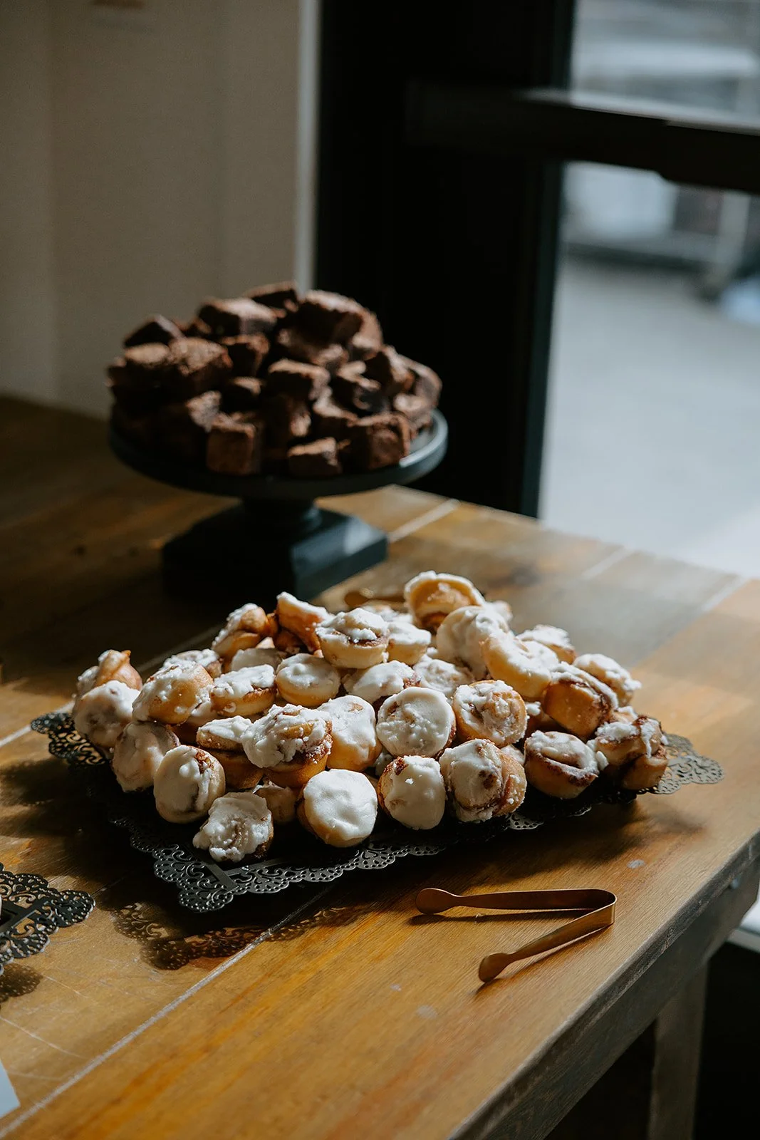 Assorted iced pastries on a decorative serving tray with chocolate brownies on a cake stand behind them.