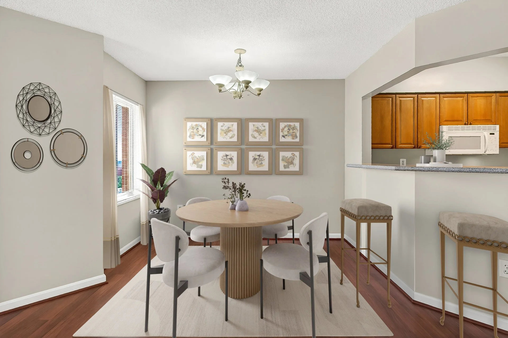 Dining room with round wooden table, six white chairs, and greenery centerpiece. Wall decor includes framed art and three circular metal wall hangings. Window with blinds, hardwood floor, and an open kitchen with wood cabinets and white appliances.