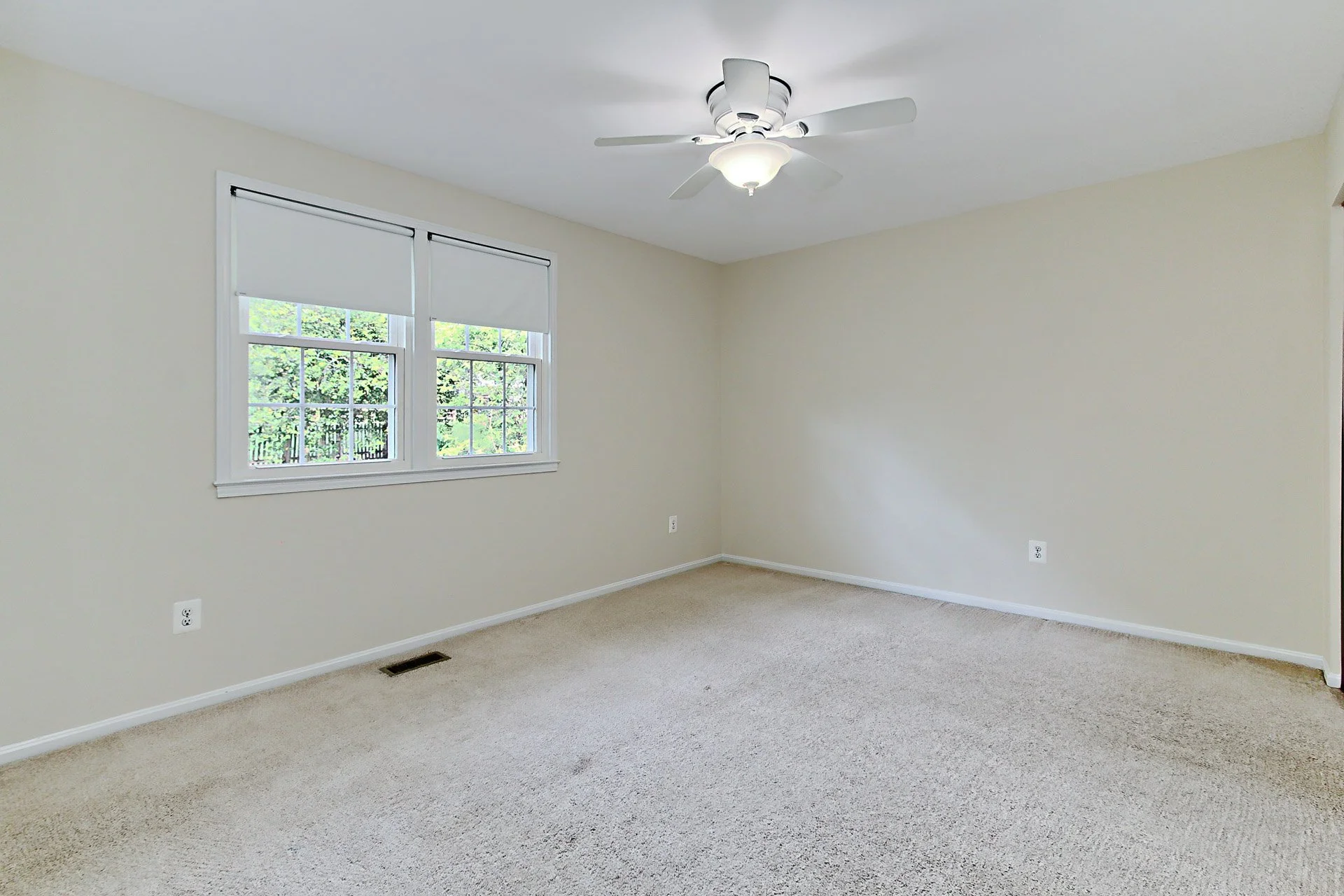 Empty room with beige carpet, off-white walls, two windows with blinds, ceiling fan with light, and multiple electrical outlets.