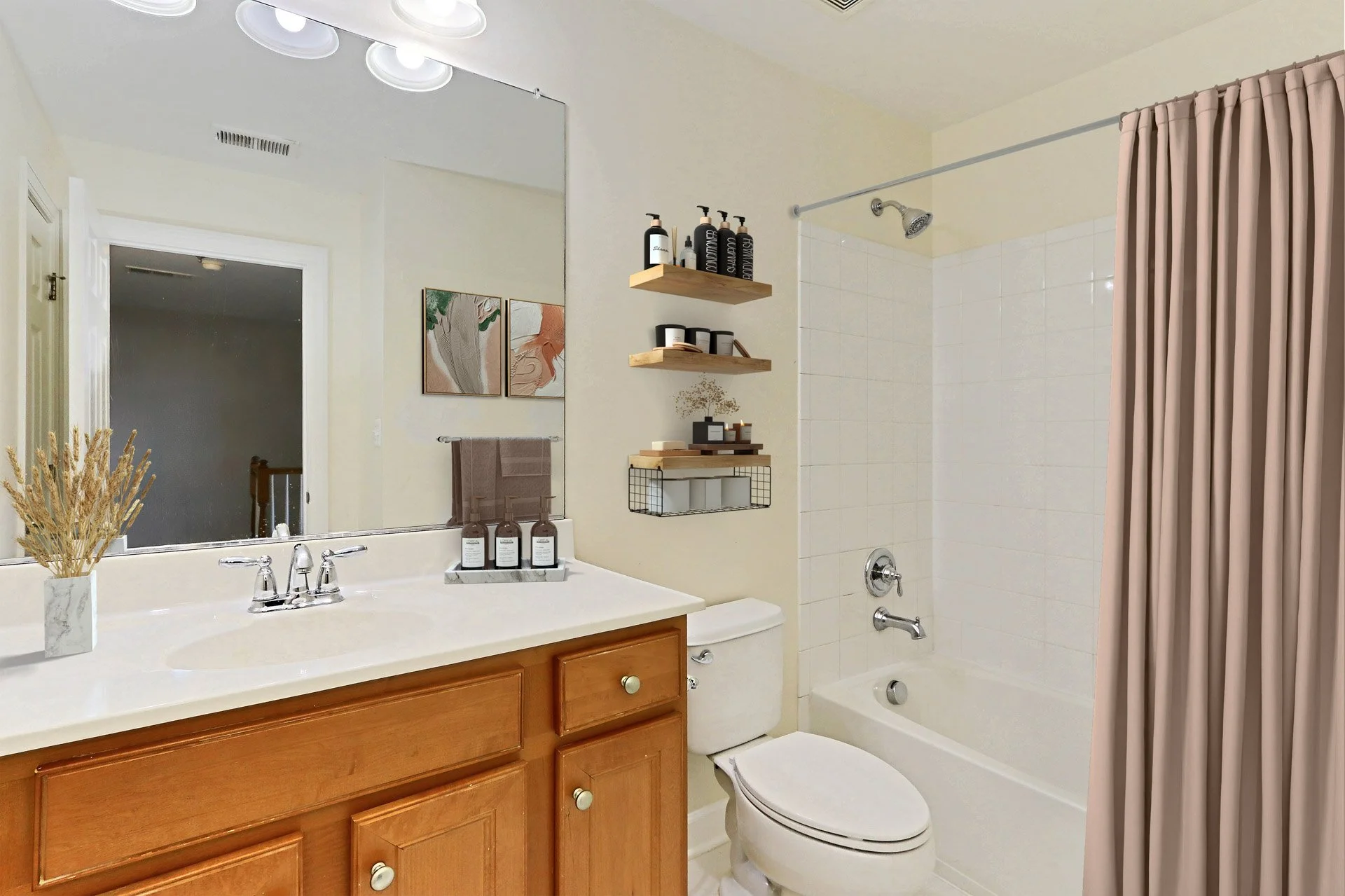 Bathroom with wooden vanity, large mirror, beige walls, white bathtub with shower head, pink shower curtain, and decorative shelves with toiletries.