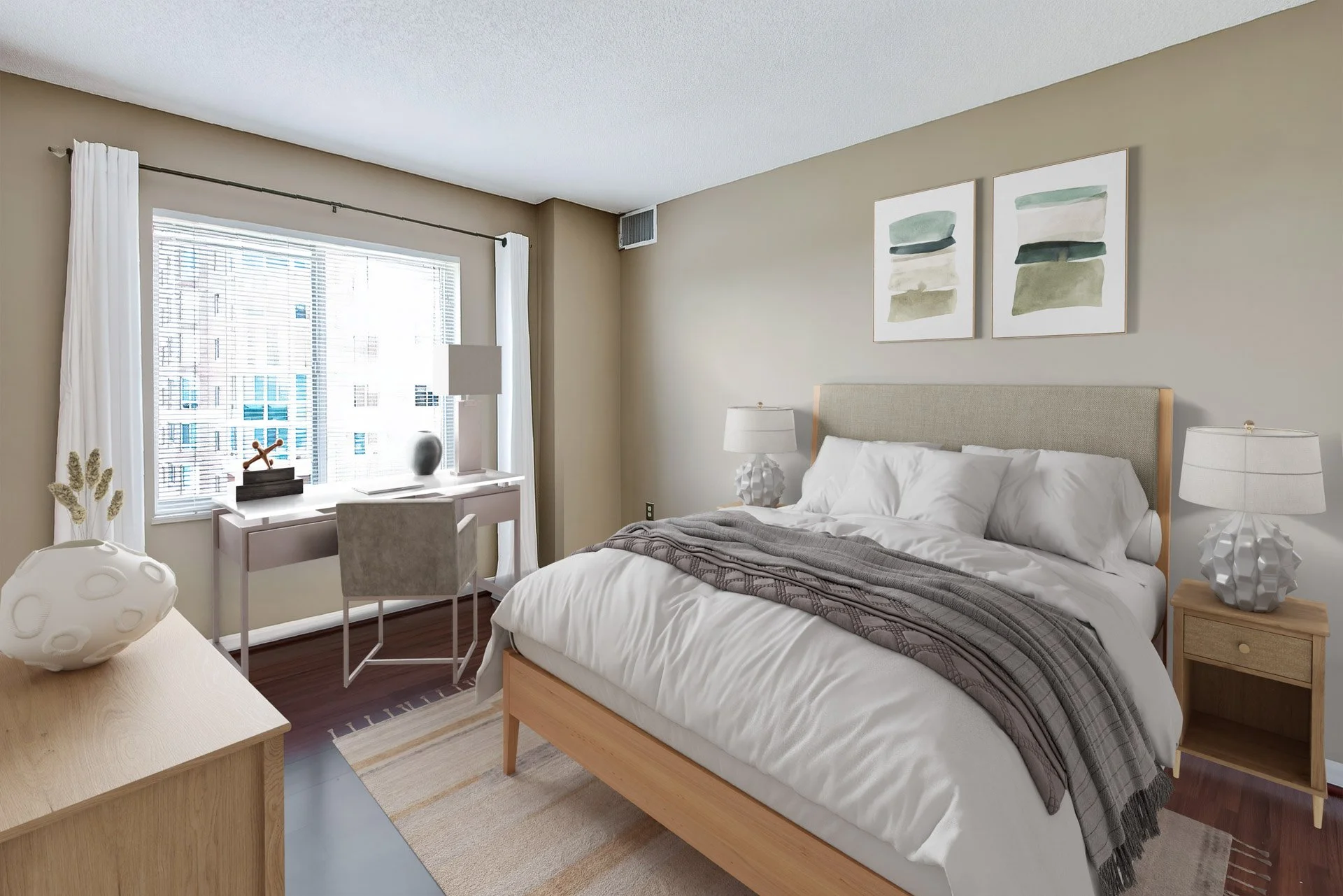 A modern bedroom with a large bed, two nightstands with matching lamps, a window with white curtains, a small desk with a gray chair, and abstract artwork on the wall.