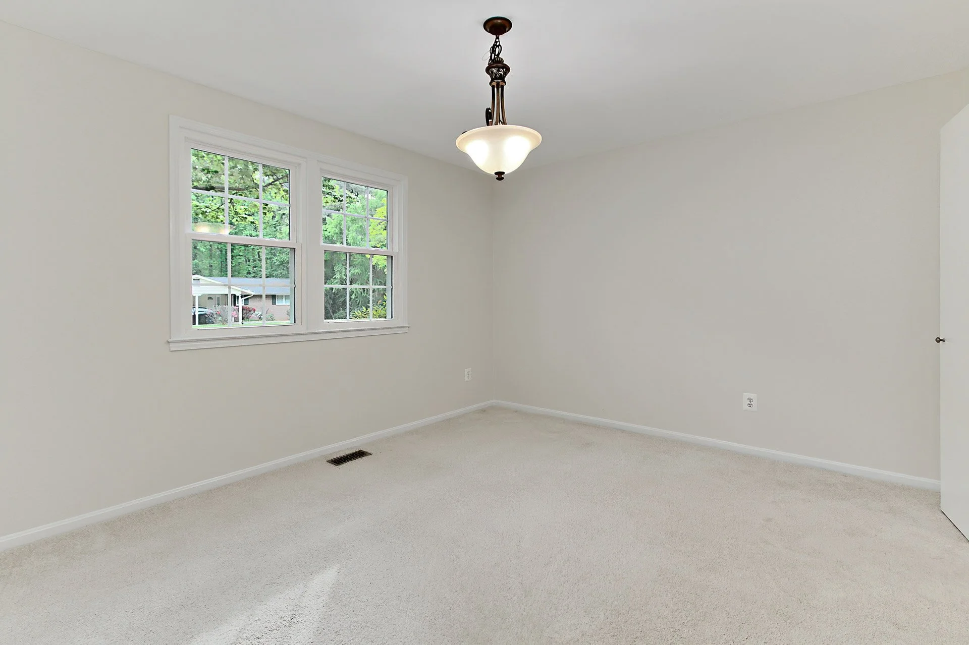 Empty room with beige carpet, white walls, two windows, and a ceiling light fixture.