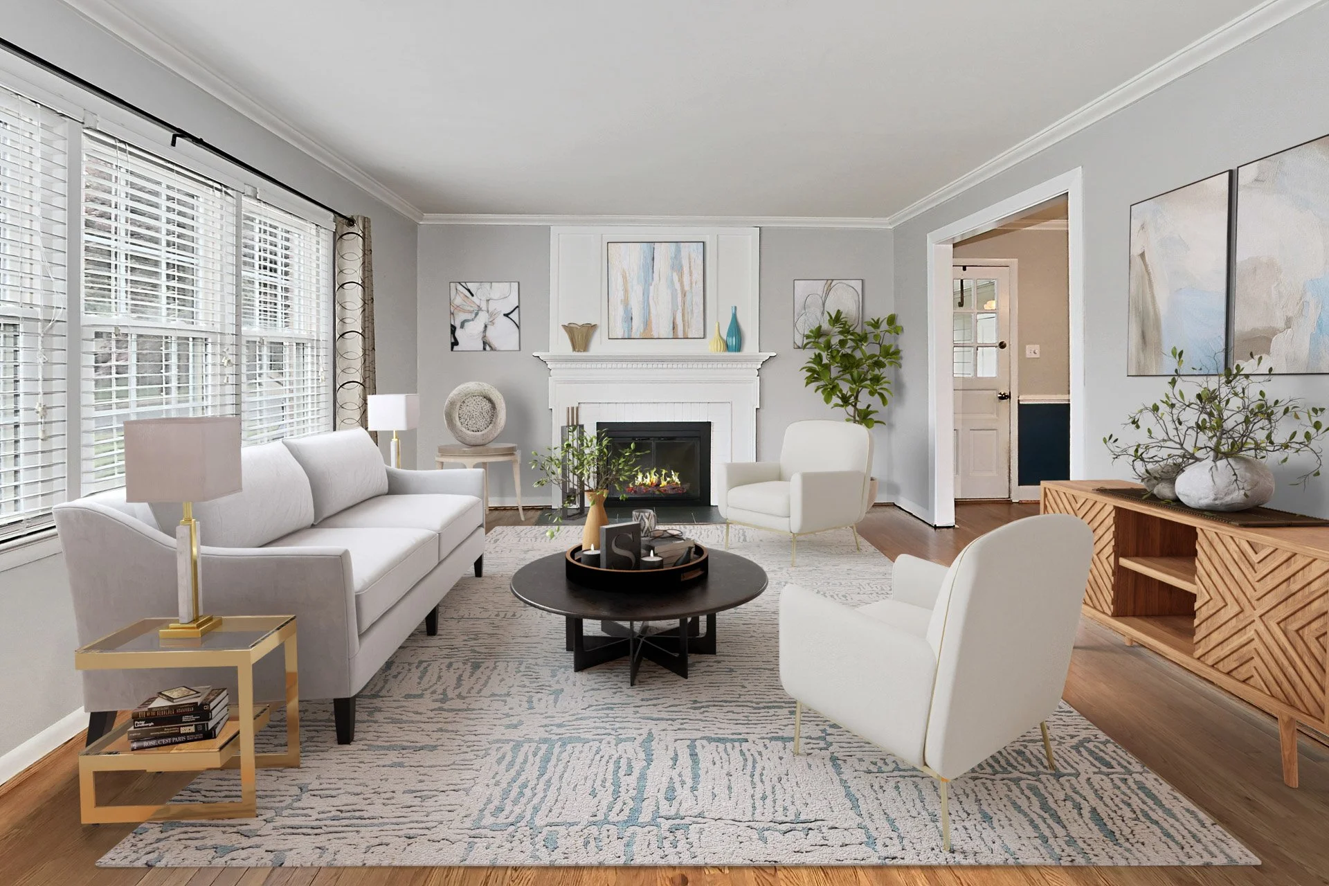 Living room with white sofa and chairs, fireplace, large windows with blinds, wooden sideboard with plant, coffee table with decor, area rug, and abstract artwork.