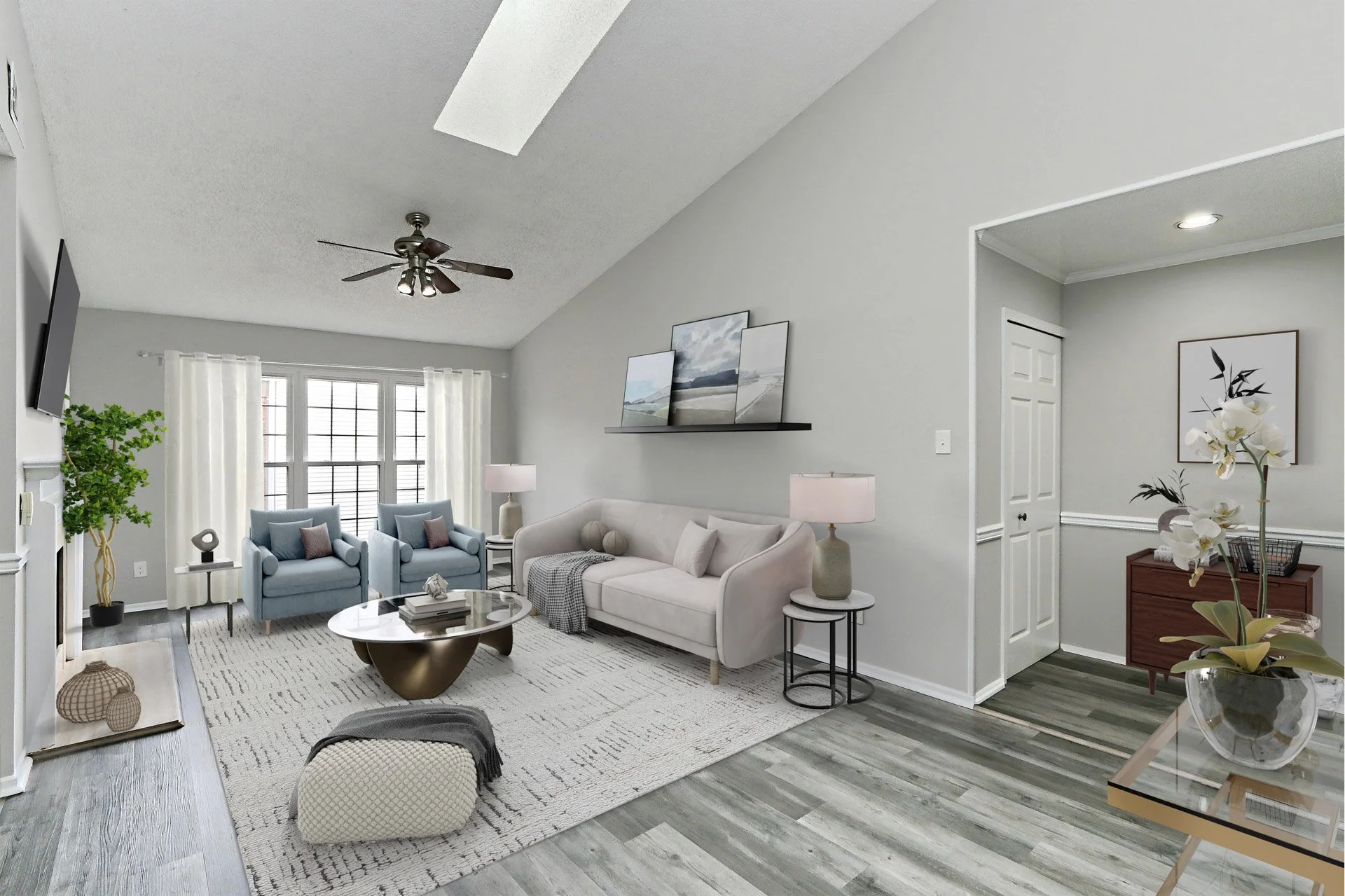 Living room with light gray walls, white curtains, a white sofa, two blue armchairs, a round coffee table, lamps, and wall art. There is a ceiling fan, hardwood flooring, and a large window letting in natural light.