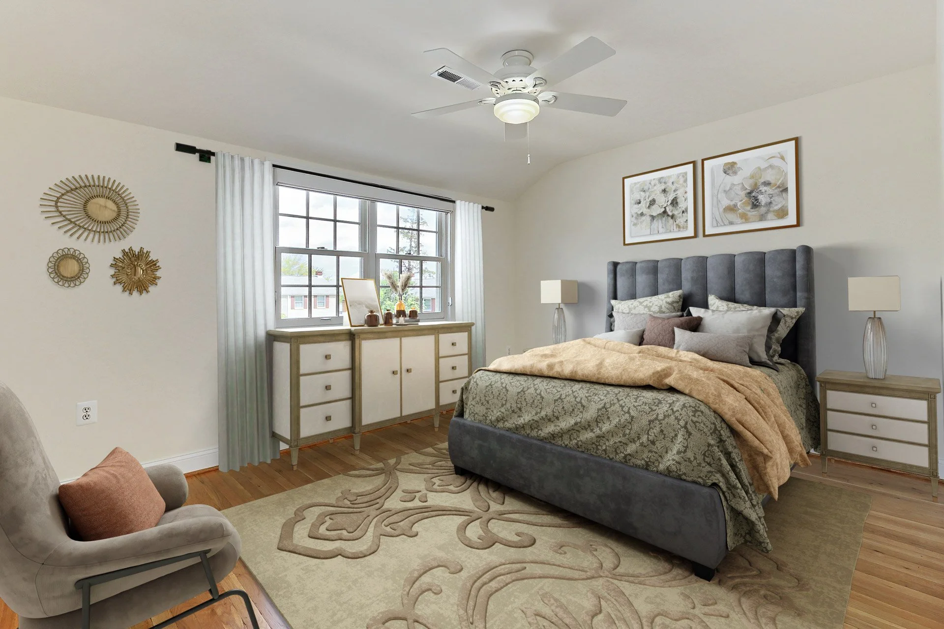 A bedroom with a large window, gray upholstered bed, nightstands with lamps, and framed artwork above the bed. There is a beige area rug, a gray armchair with a pillow, and decorative wall art.