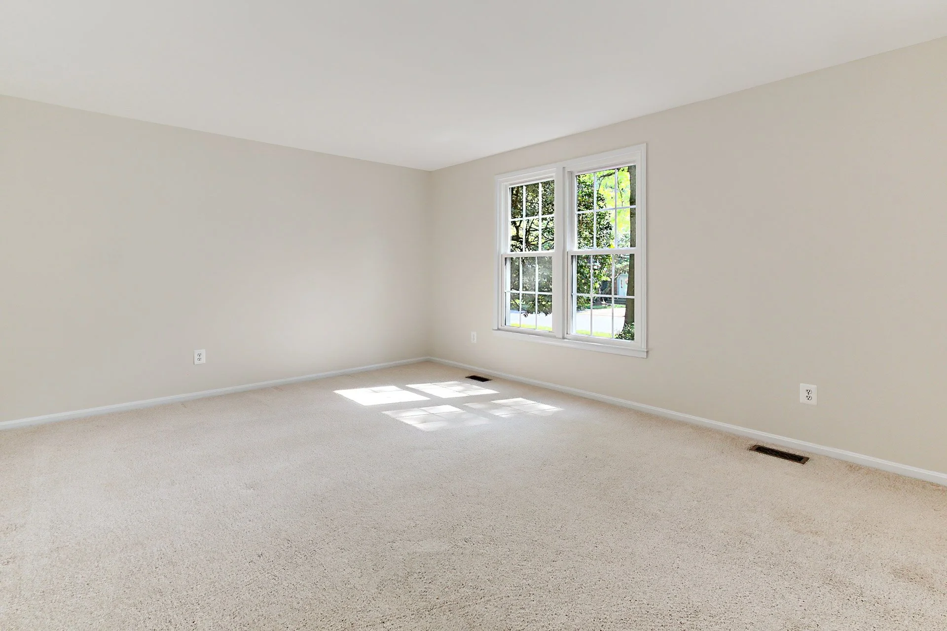 Empty room with white walls, beige carpet, and a large window letting in natural light.