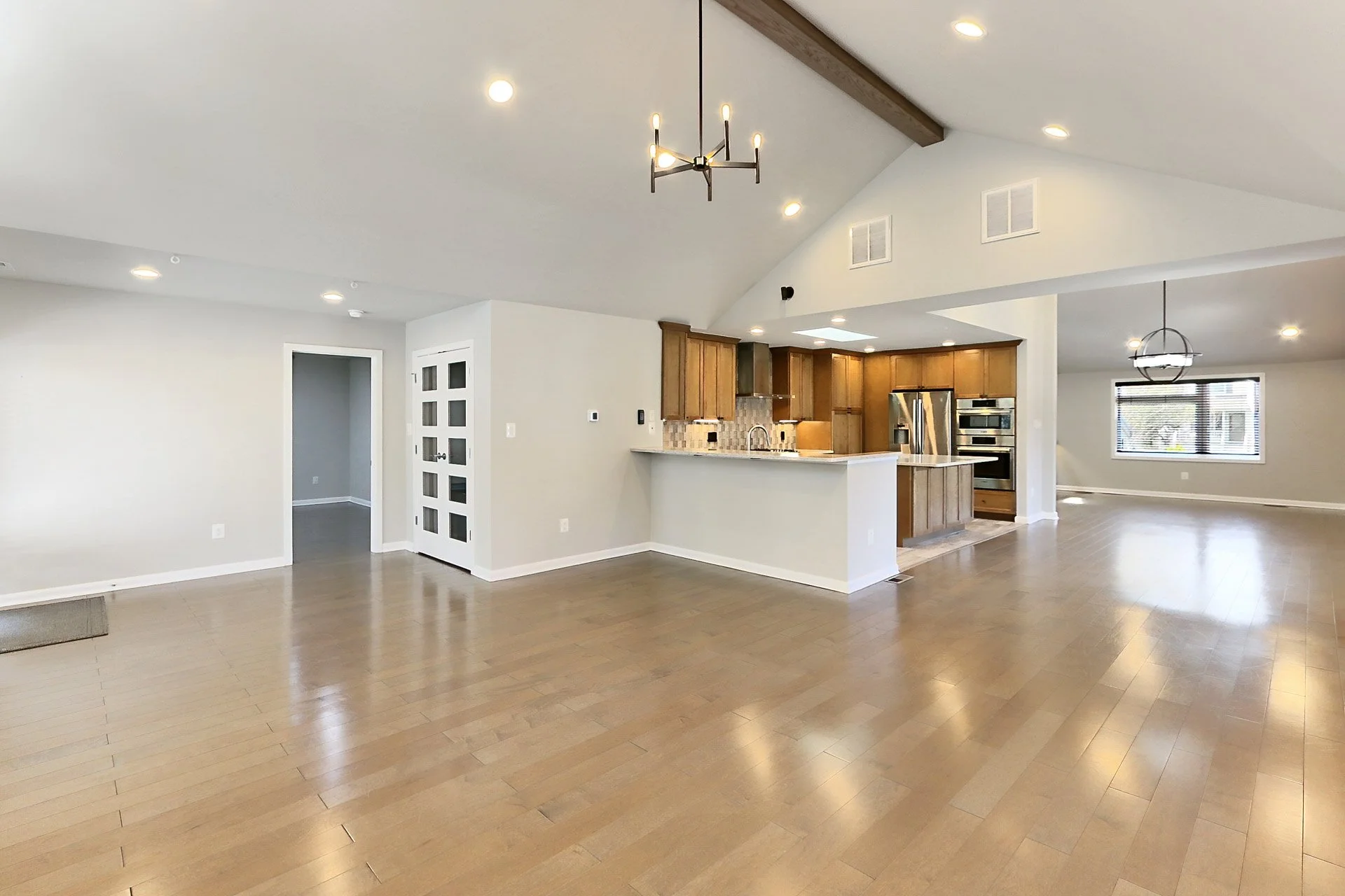 Open-concept living space with hardwood floors, a modern kitchen with wooden cabinets, a breakfast bar, and stainless steel appliances, and a large window letting in natural light.