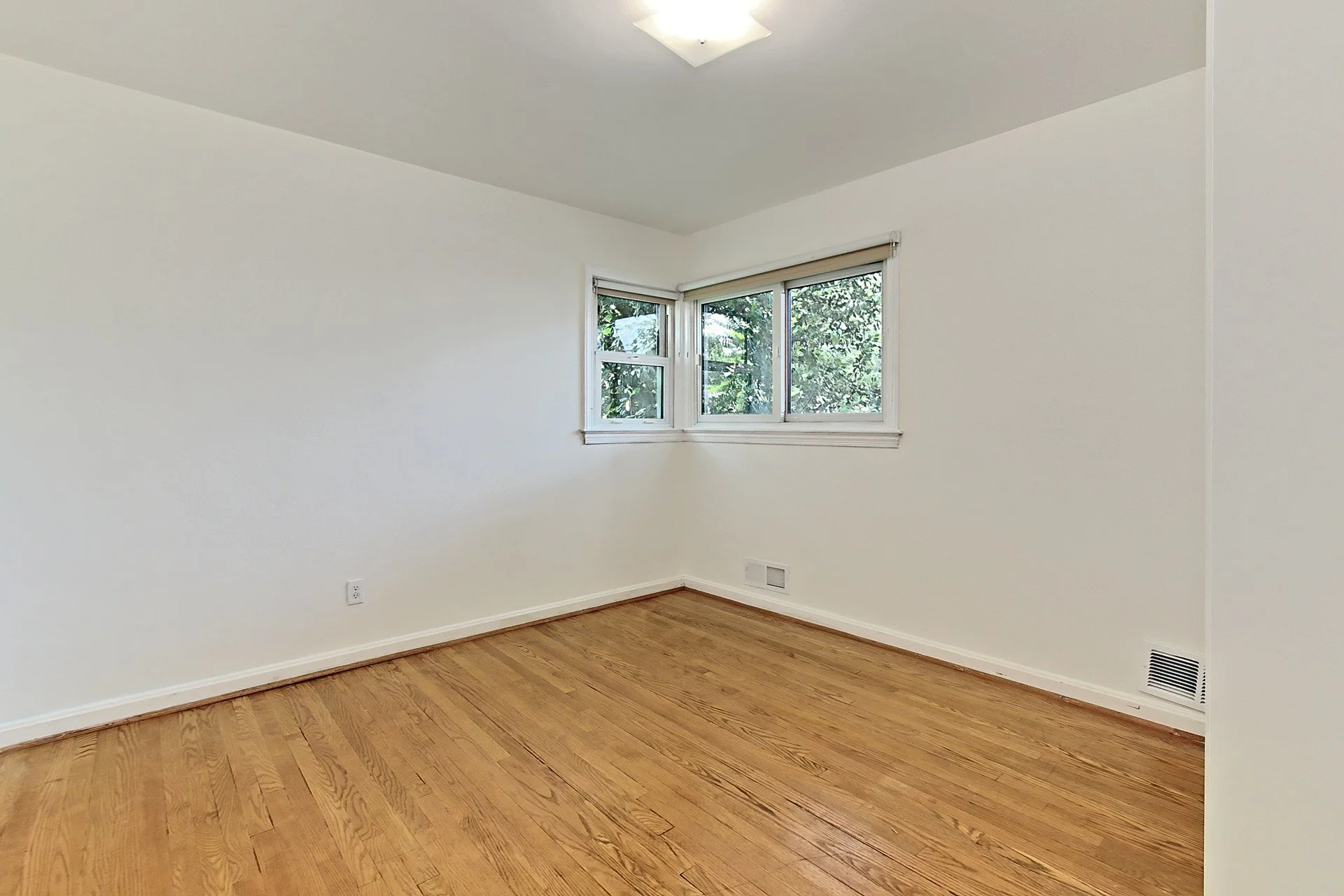 Empty room with white walls, hardwood floor, three windows, and a ceiling light.