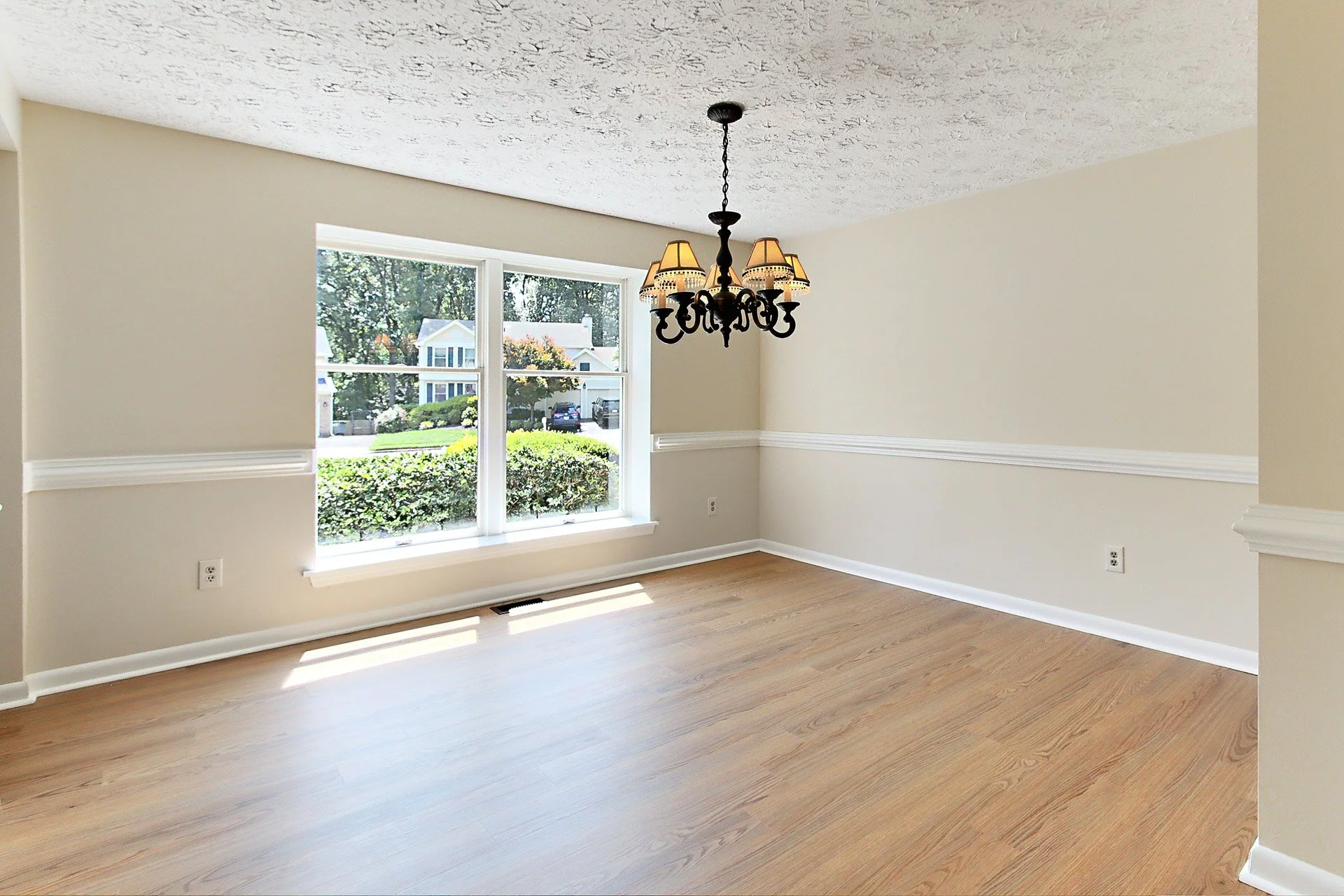 Empty dining room with large window, wooden floors, and chandelier light fixture.