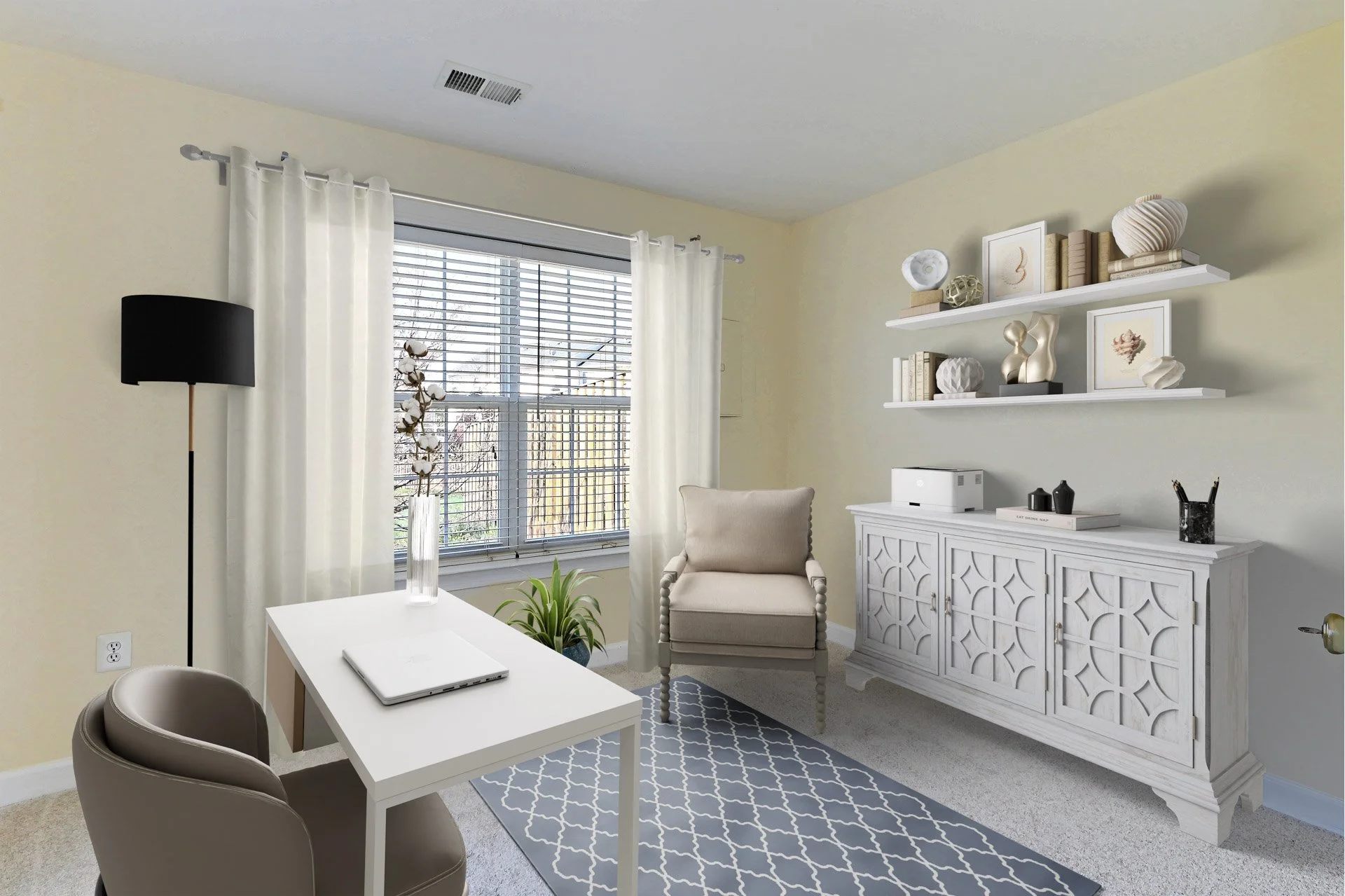Home office with white furniture, a beige armchair, a white desk with a laptop, and decor on shelves, near a window with blinds and curtains.