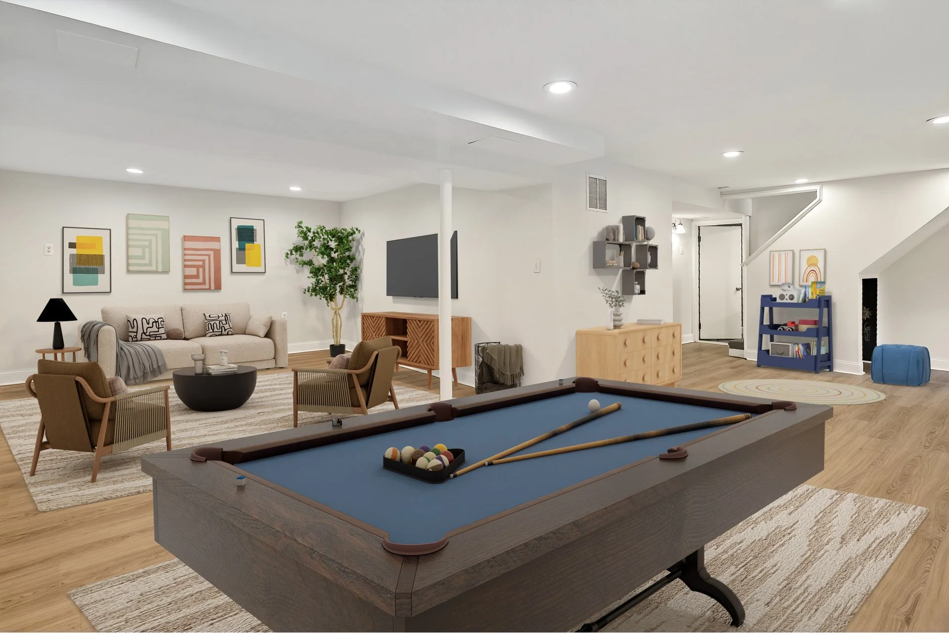 A spacious, modern basement living room with a pool table in the foreground, a beige sofa with decorative pillows, two armchairs, a TV on a wooden stand, a small shelving unit with books, colorful wall art, potted plants, and children's toys and play