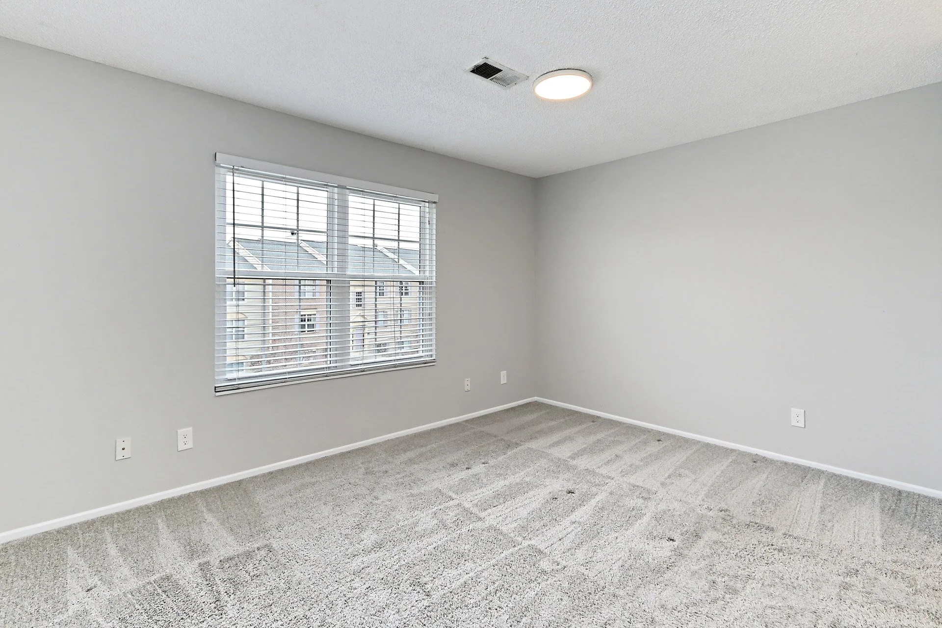 An empty room with white walls, a window with blinds, a textured ceiling, carpet flooring, and ceiling light fixture.