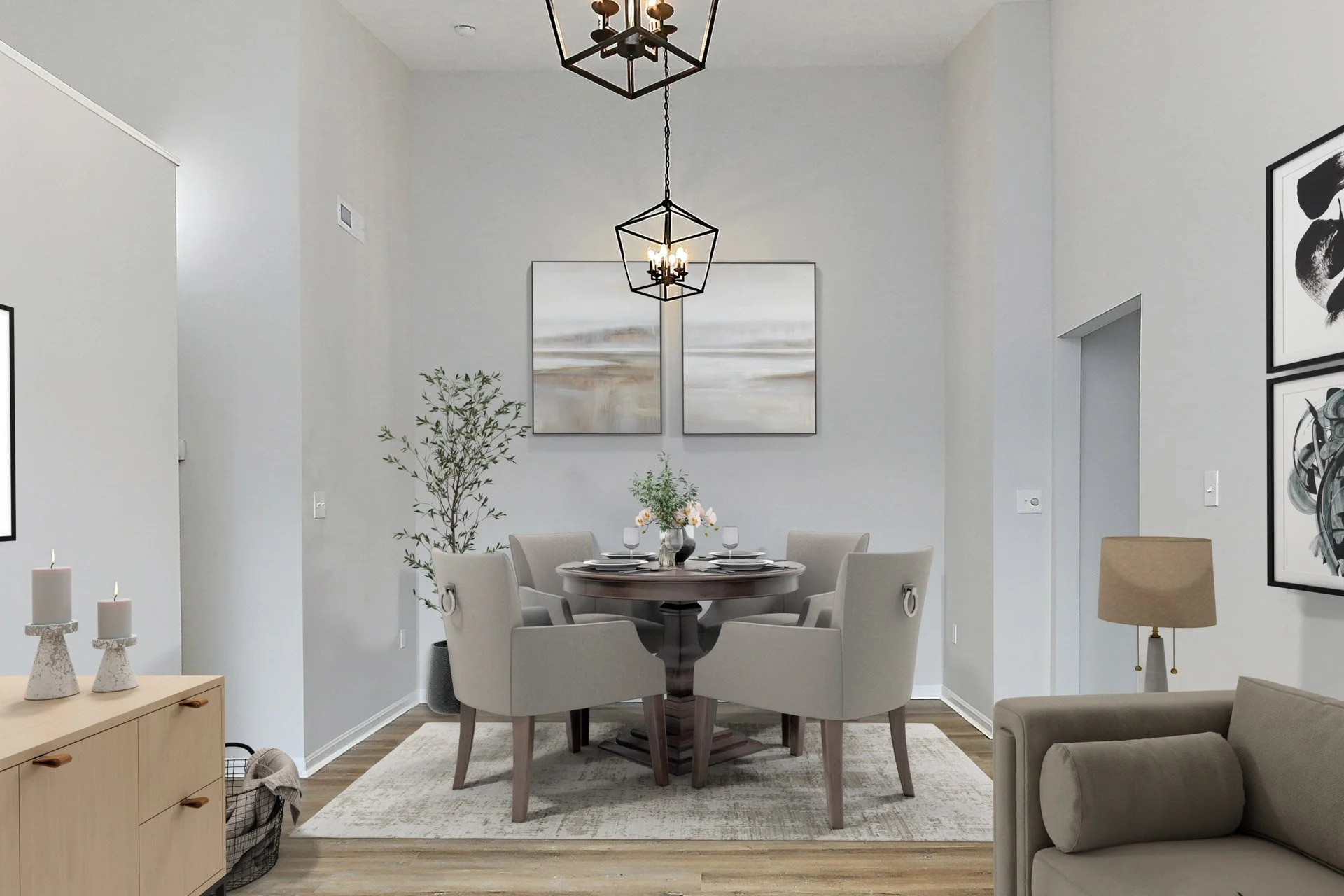 A modern dining room with a round table, six beige upholstered chairs, wall art, a vase with flowers, candles, a wooden sideboard, a painting of abstract art, a floor lamp, a beige couch, and a ceiling light with a black geometric frame.