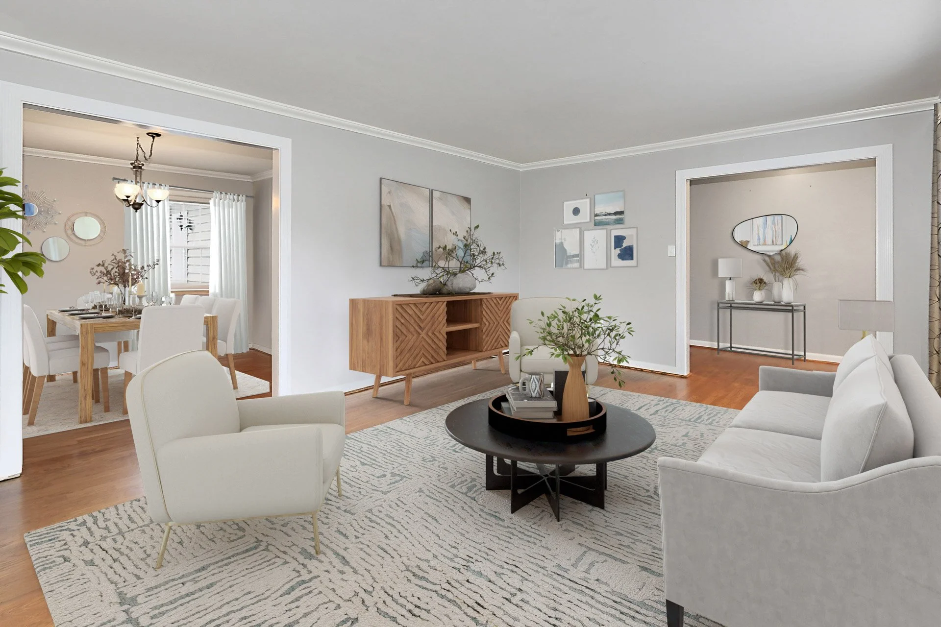 Living room with white sofa, armchair, black coffee table with a tray and plant, artwork on light gray walls, hardwood floors, and adjacent dining room with white chairs and wooden table.