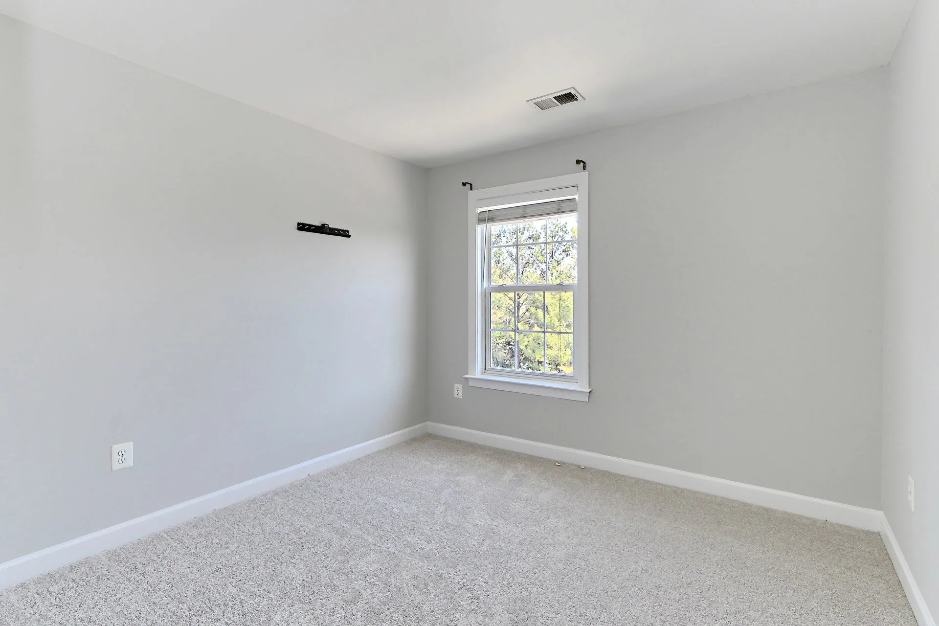Empty room with a window, white walls, beige carpet, and a black wall mount.