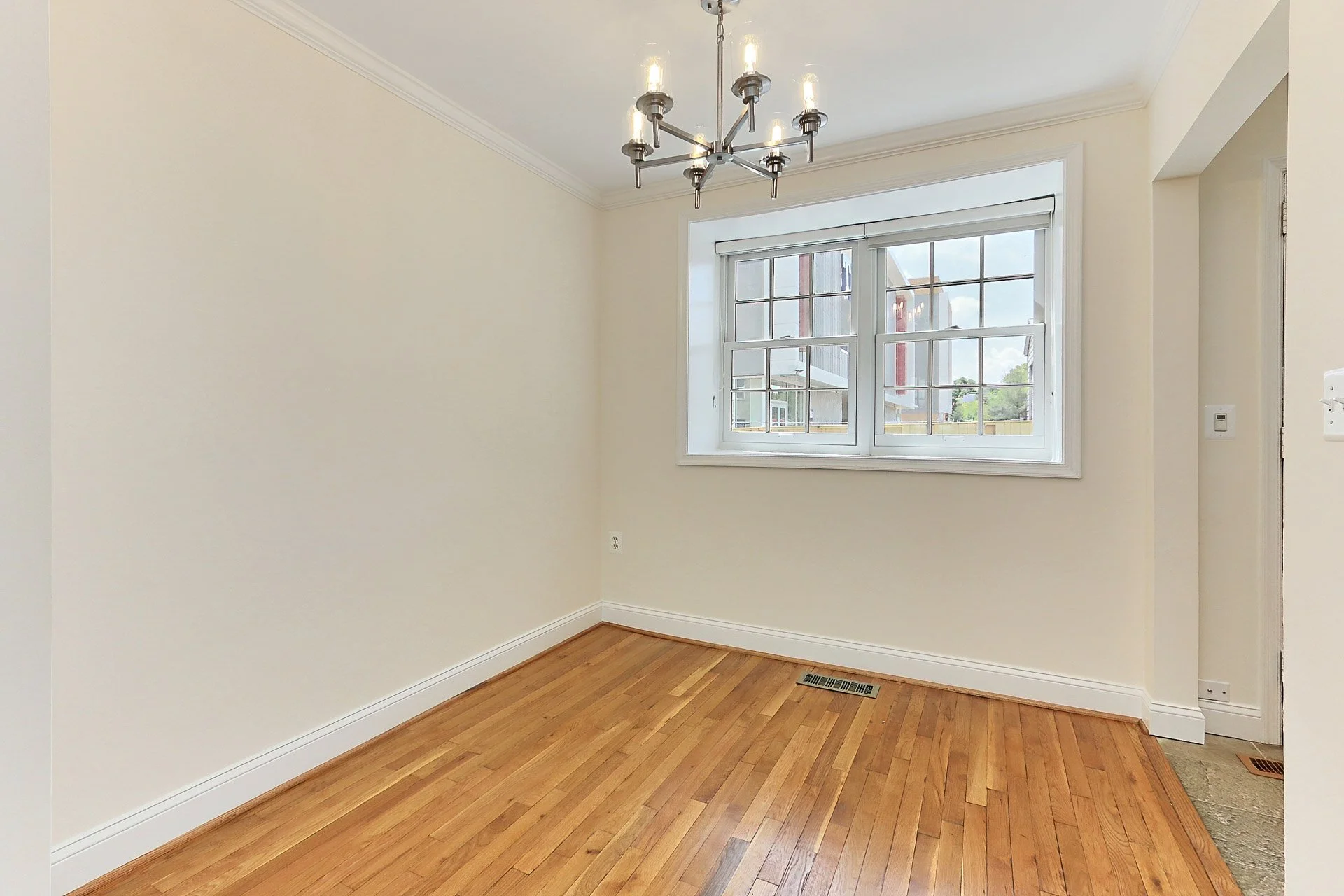 Empty room with hardwood floors, white walls, a window, crown molding, and a modern chandelier.