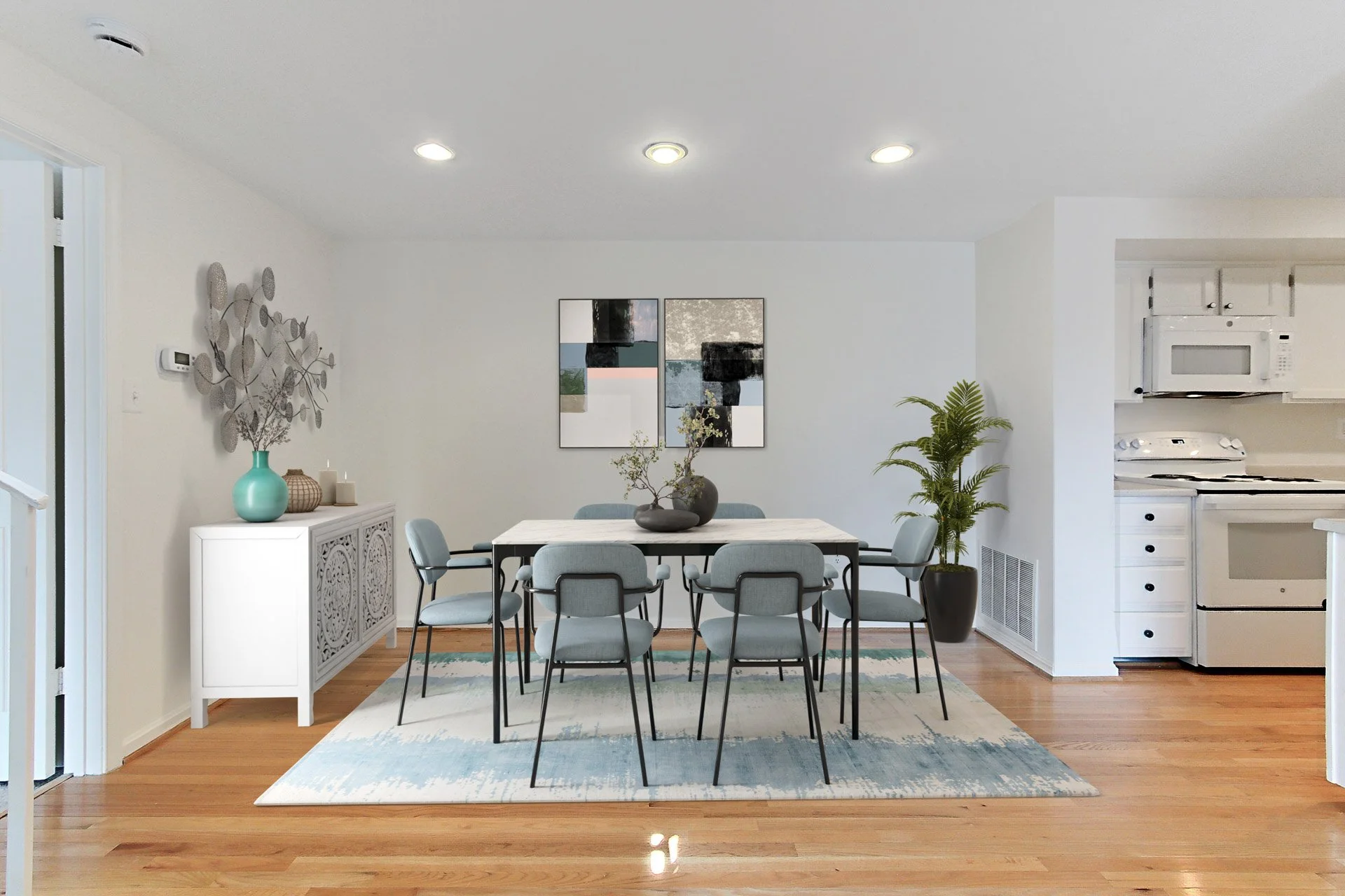 Dining room with light wood flooring, white walls, and a black and white dining table surrounded by nine light blue chairs. A colorful abstract painting hangs on the wall, and decorative items such as vases and a sculpture are on a white sideboard. A